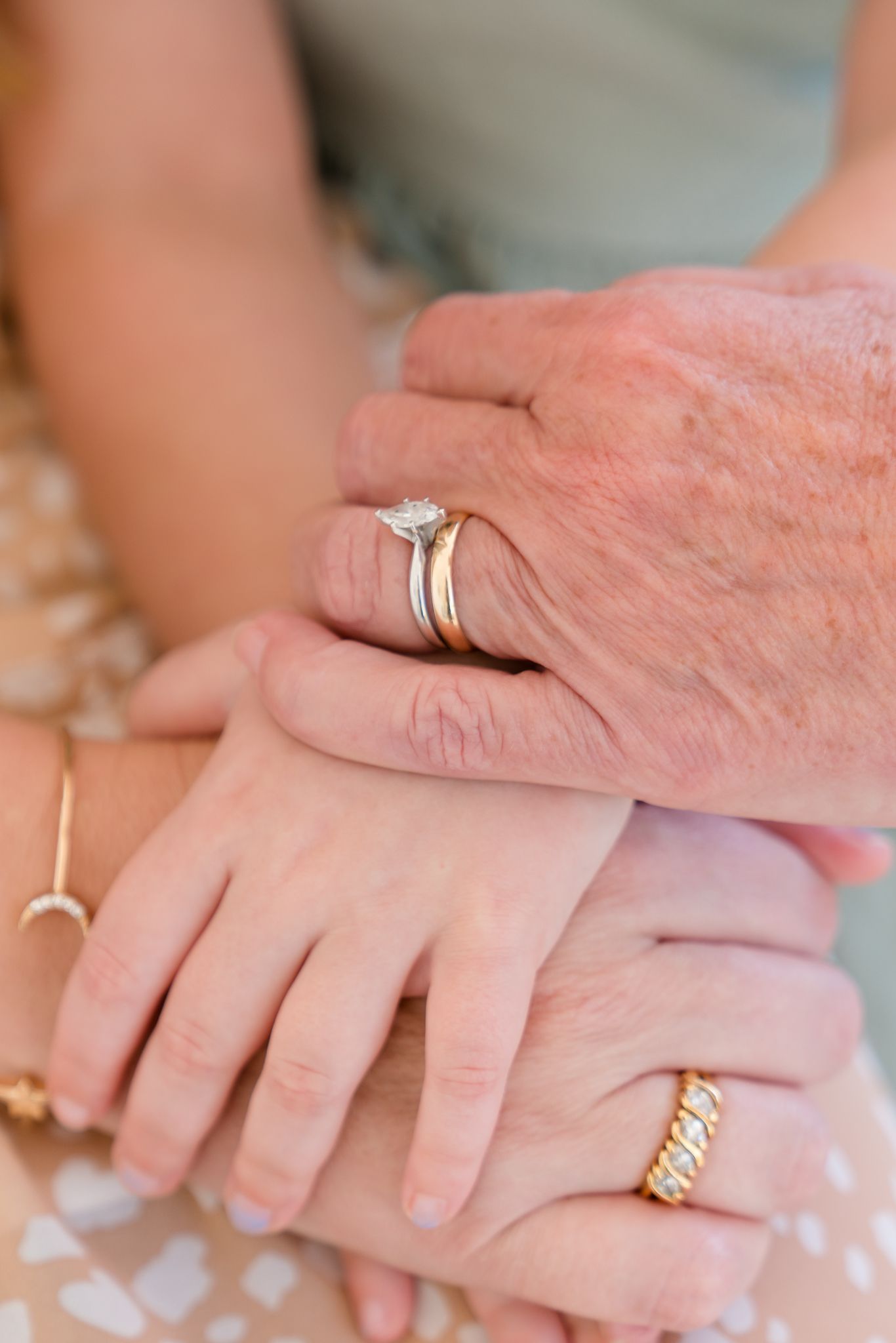 Close-up of stacked hands showing gold diamond engagement ring, wedding band, and gold ring across generations.