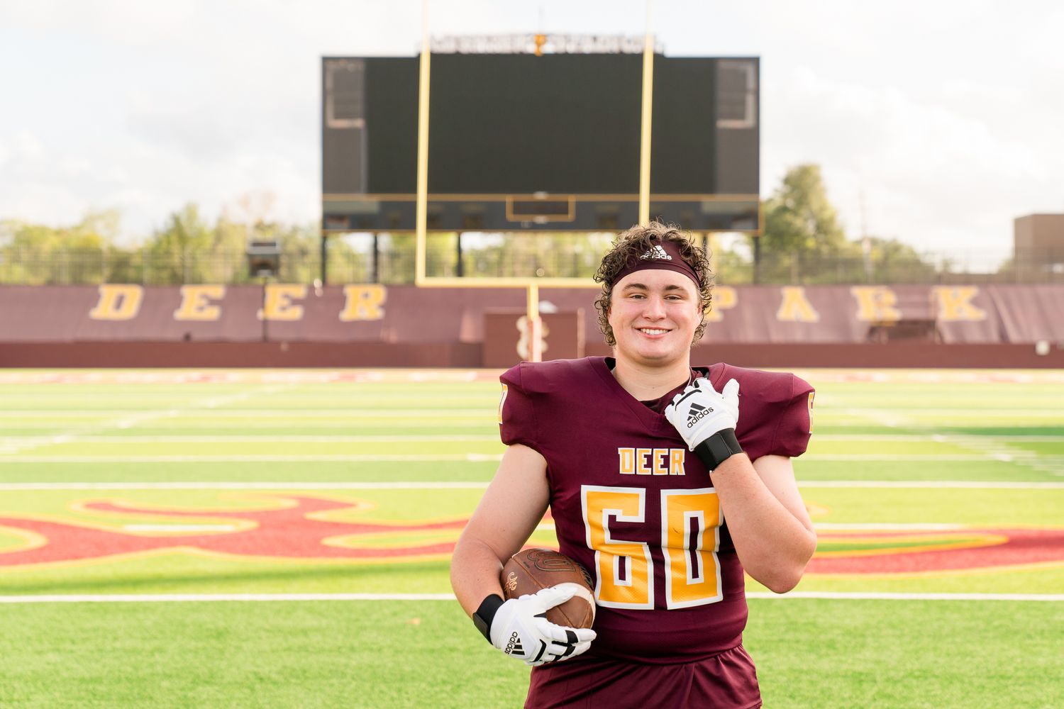 Football player in maroon jersey number 60 poses on field at Deer Park stadium on game day.