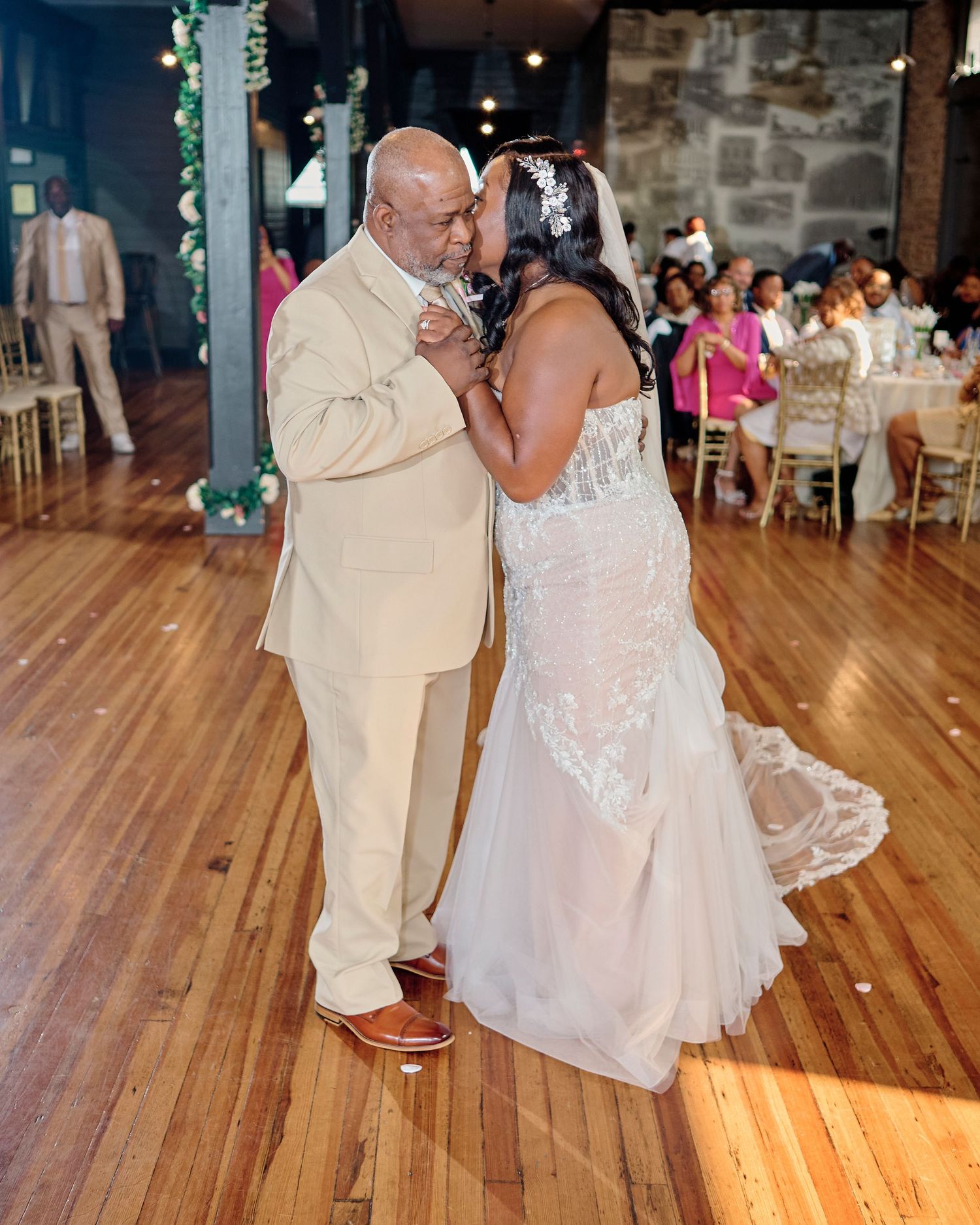 A couple shares an intimate dance moment on a wooden floor at their wedding reception.