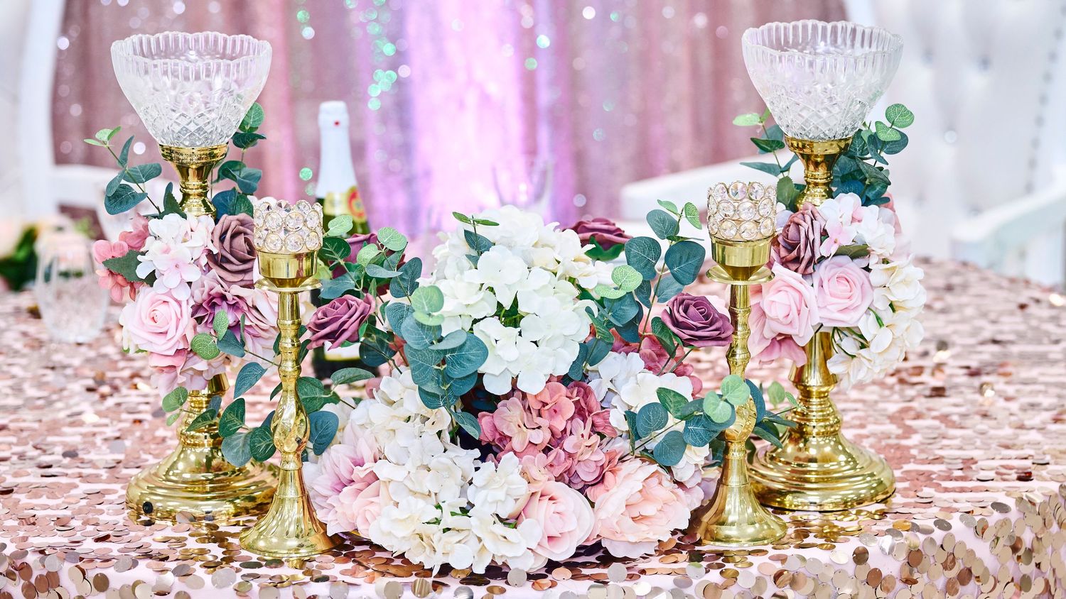 Elegant wedding table decor with gold candlesticks, pink roses, and eucalyptus on a rose gold sequined tablecloth.