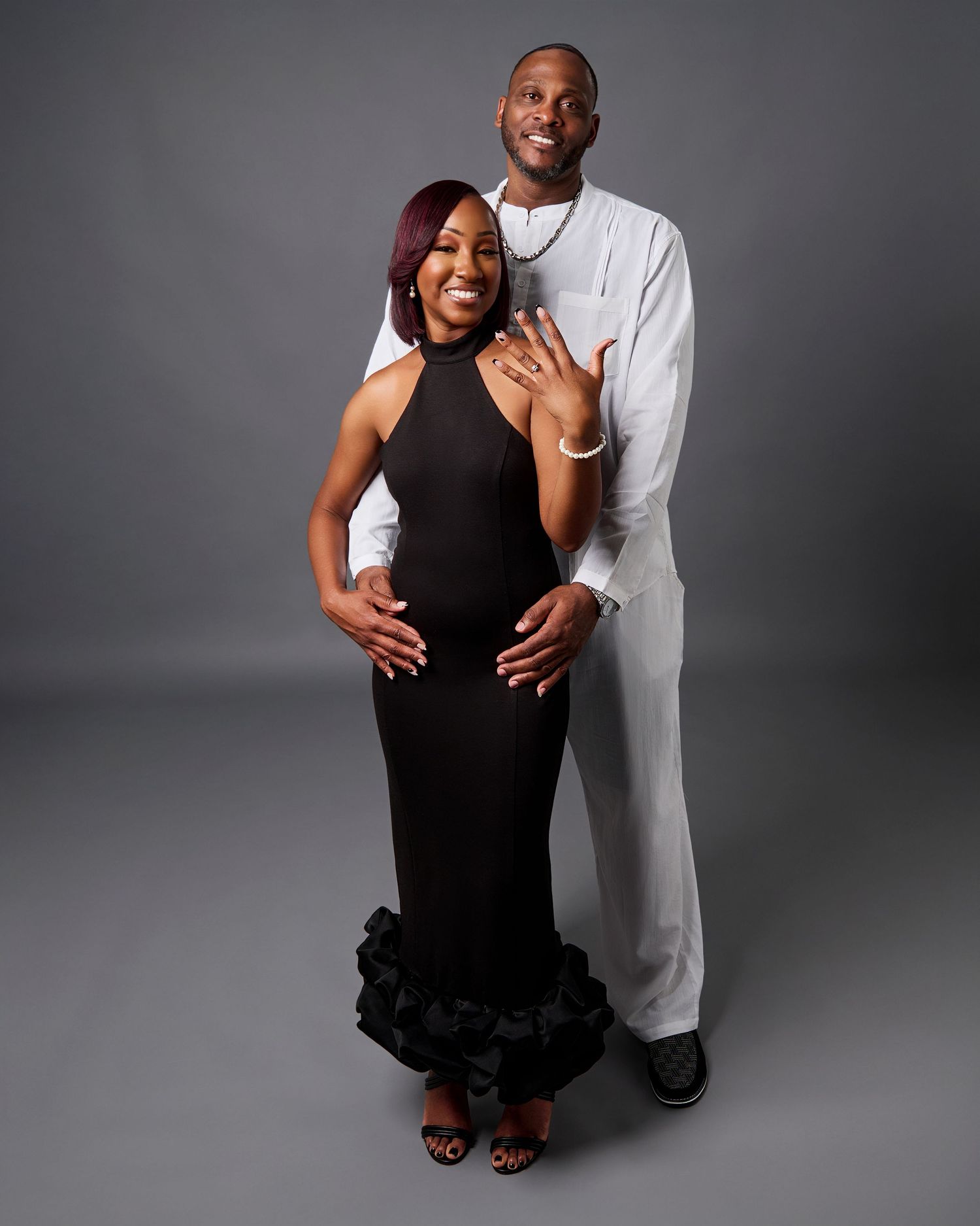 A couple poses in formal attire against a grey backdrop for an elegant portrait.