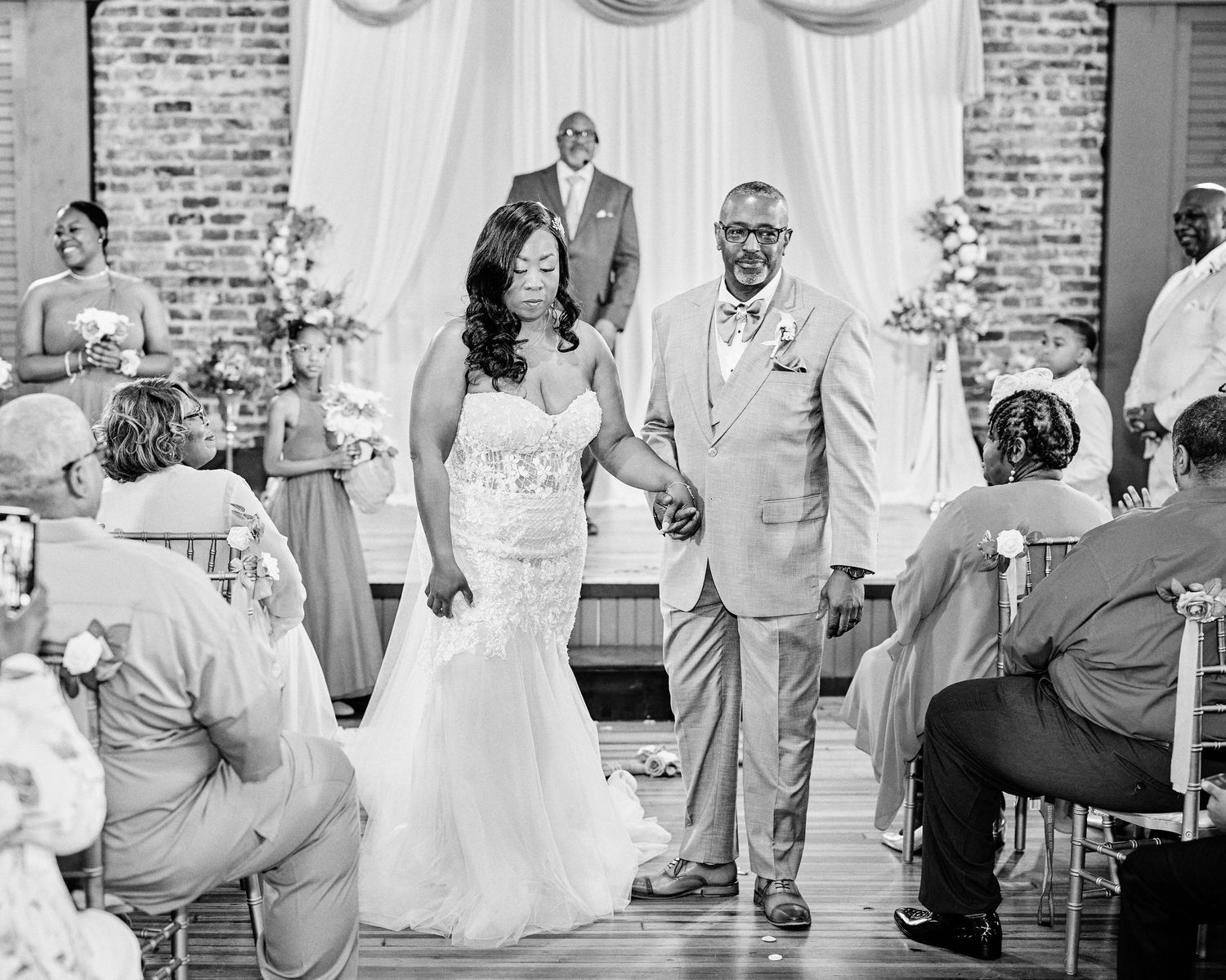 A couple celebrates their first dance in a rustic brick-walled wedding venue with white draping decor.