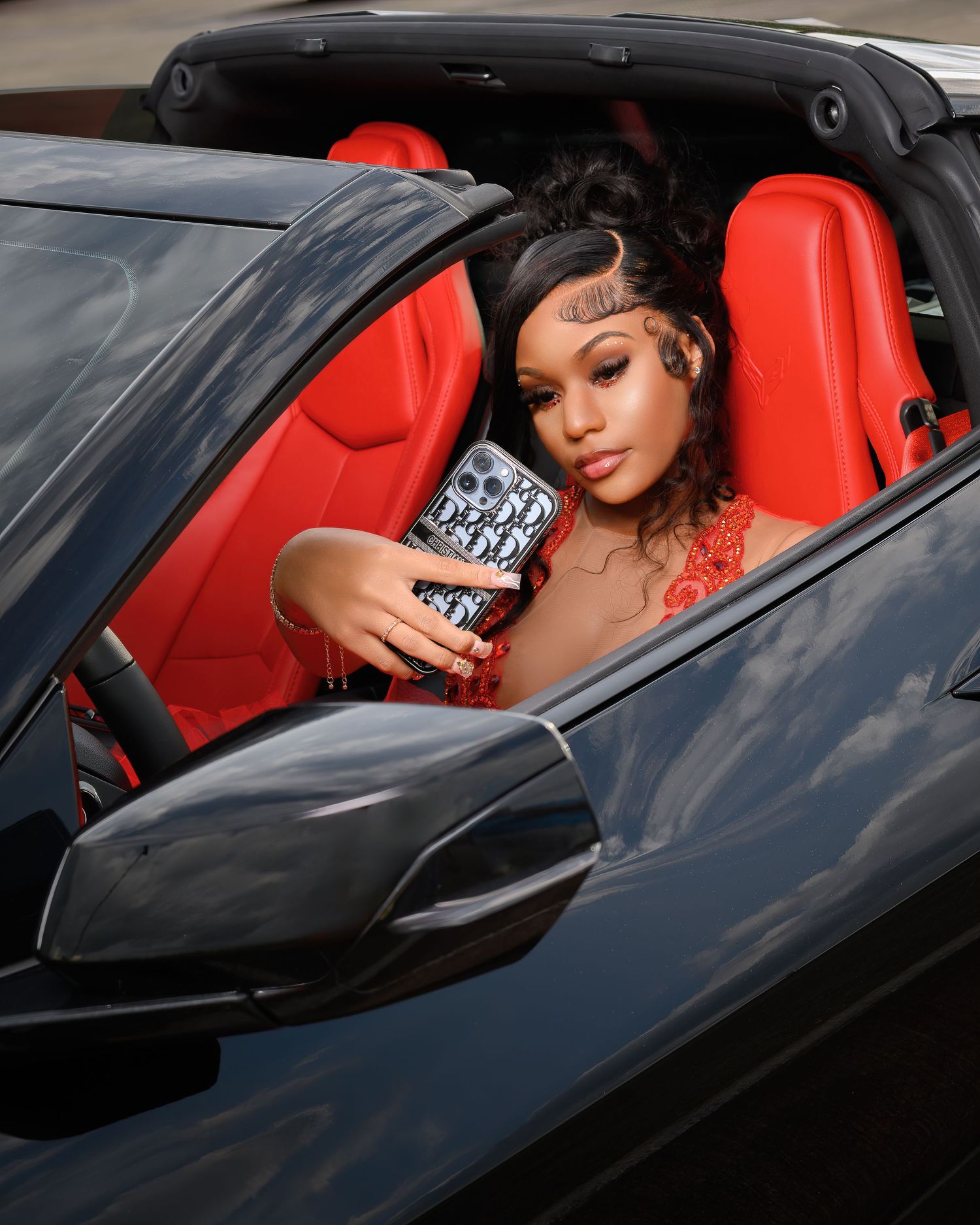 Person in sports car with red interior holds beverage while posing for lifestyle photo.