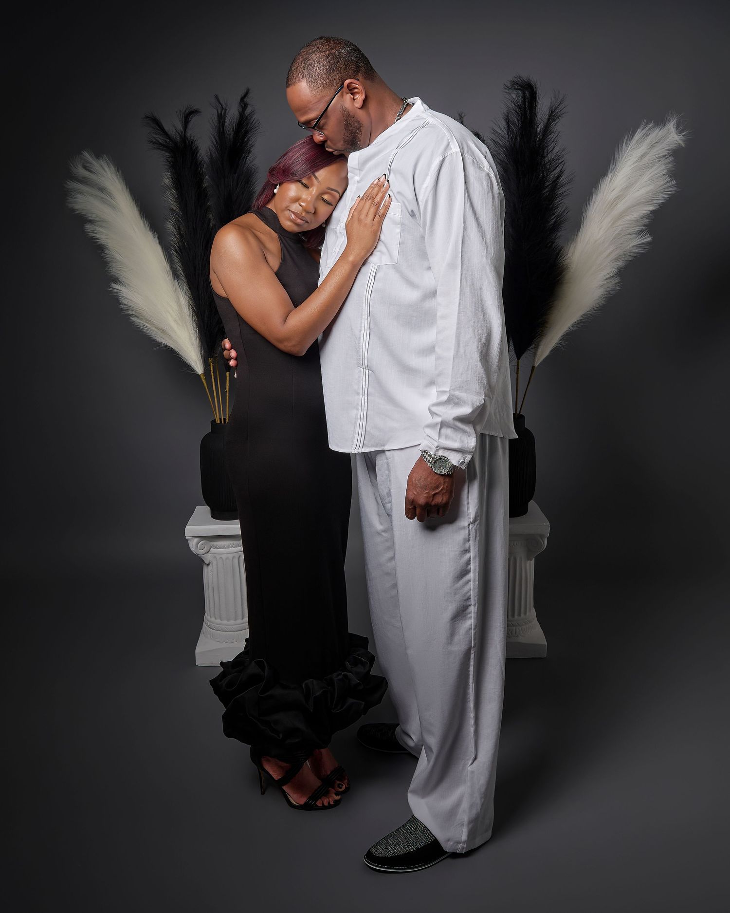 Couple in black and white formal attire share intimate dance poses against dark studio backdrop in artistic photoshoot series.