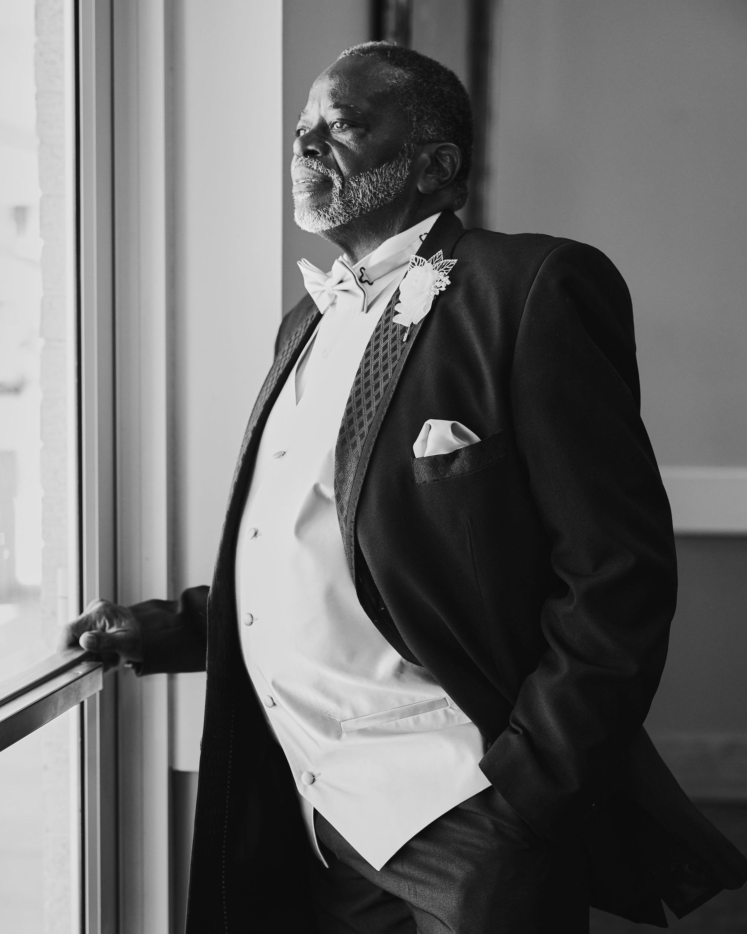 A black and white candid photo showing a person in formal wear looking thoughtfully out a window.