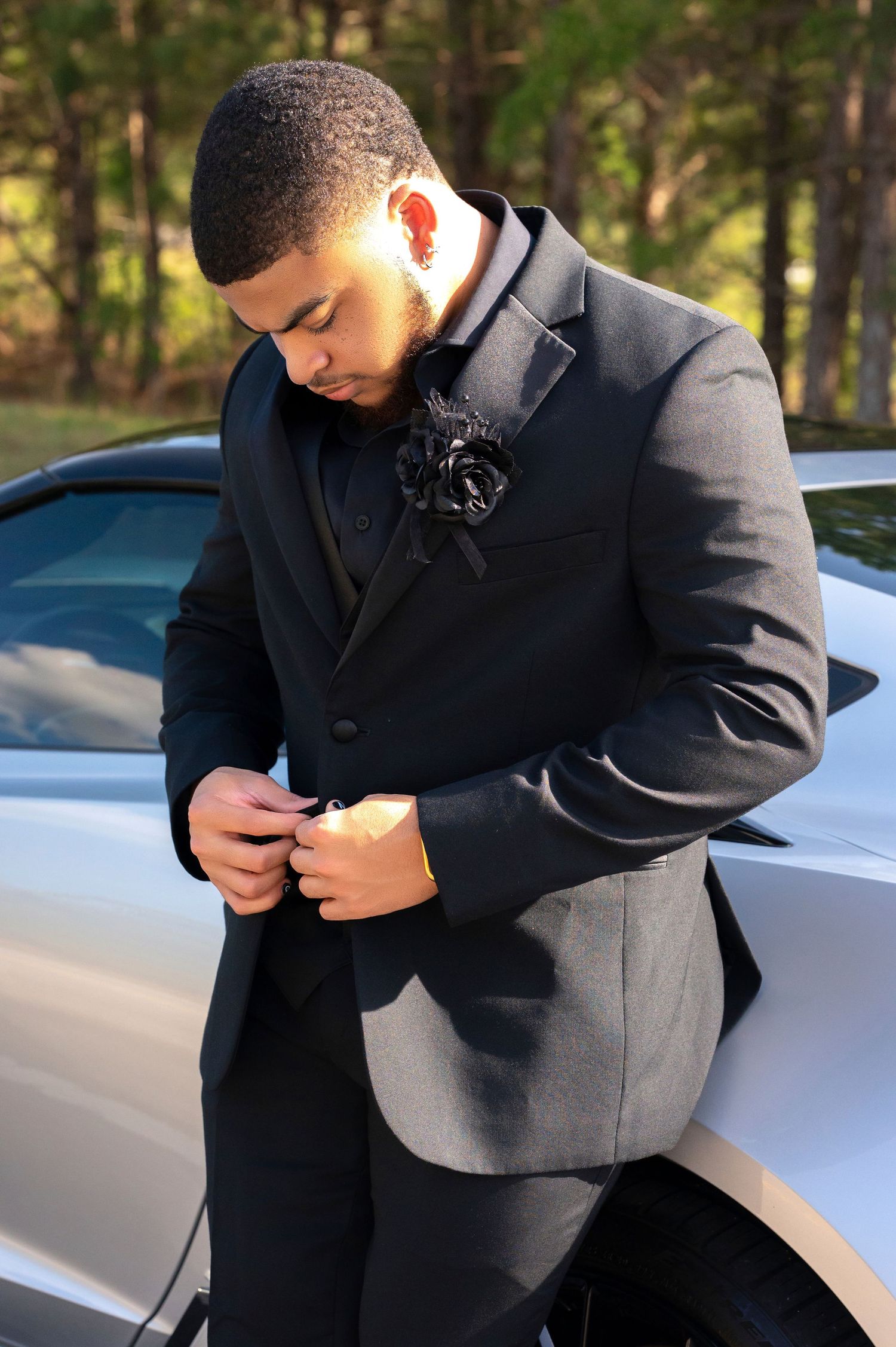 Man in gray suit adjusts buttons while standing next to silver car outdoors.