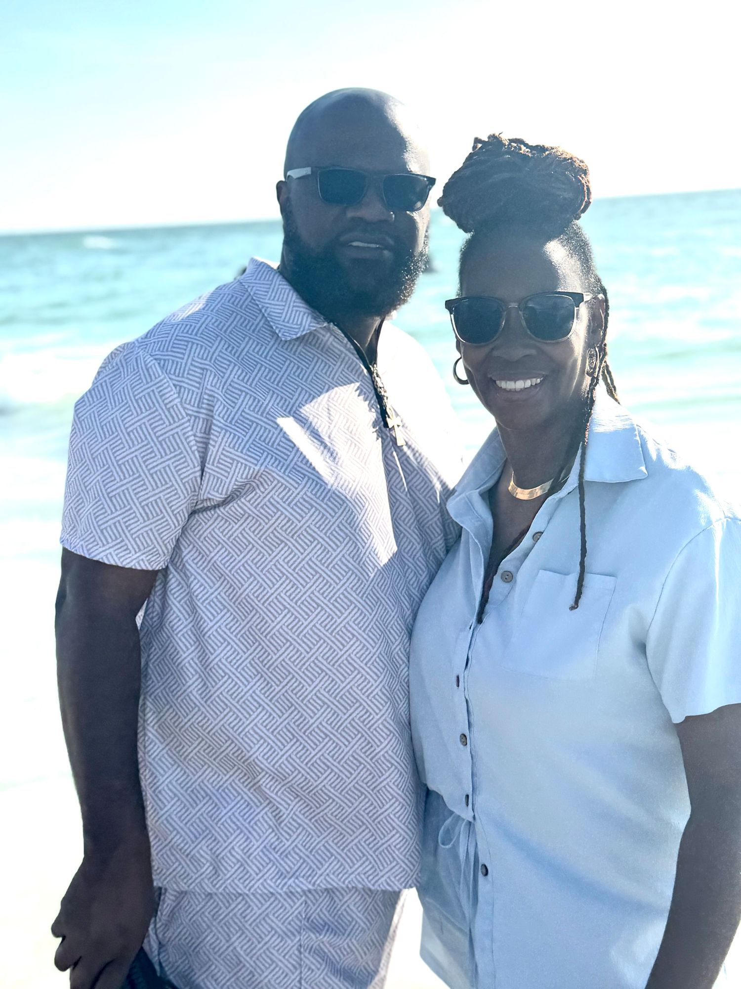 Couple smiling together on a sunny beach with bright blue ocean waters in the background.