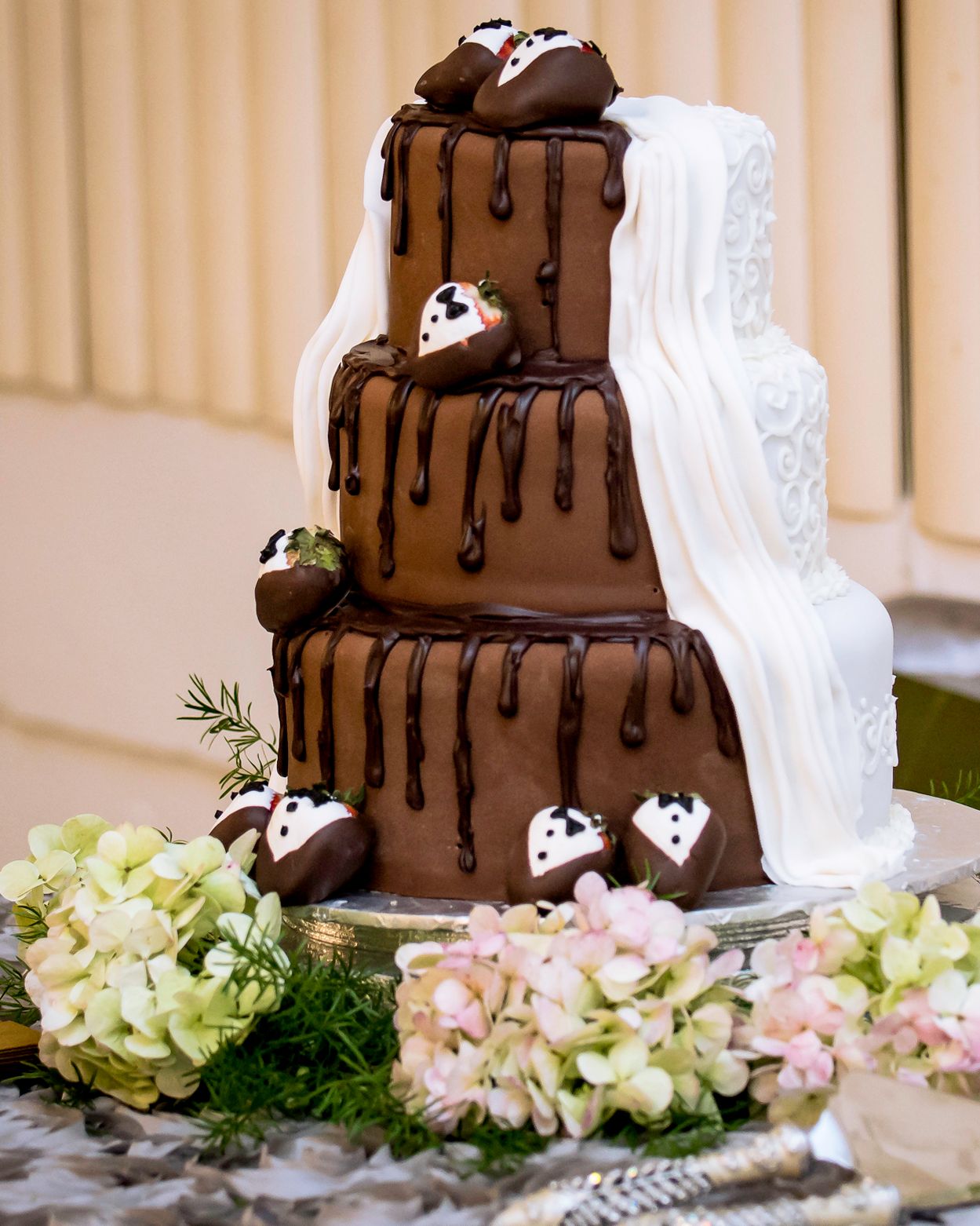 Tiered chocolate wedding cake with cascading drips and pink floral accents.