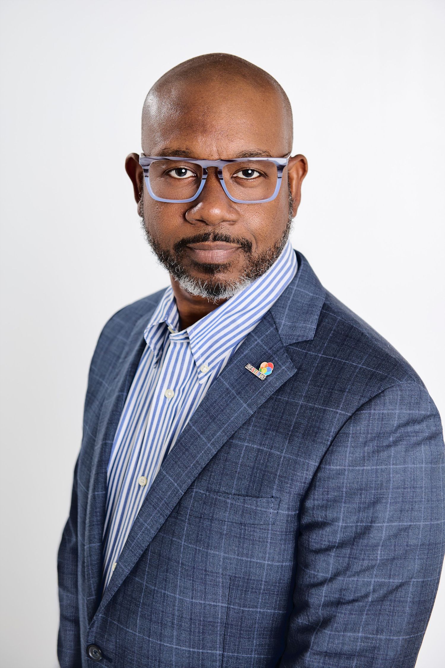 Professional headshot of businessman wearing blue plaid suit and glasses against white background.