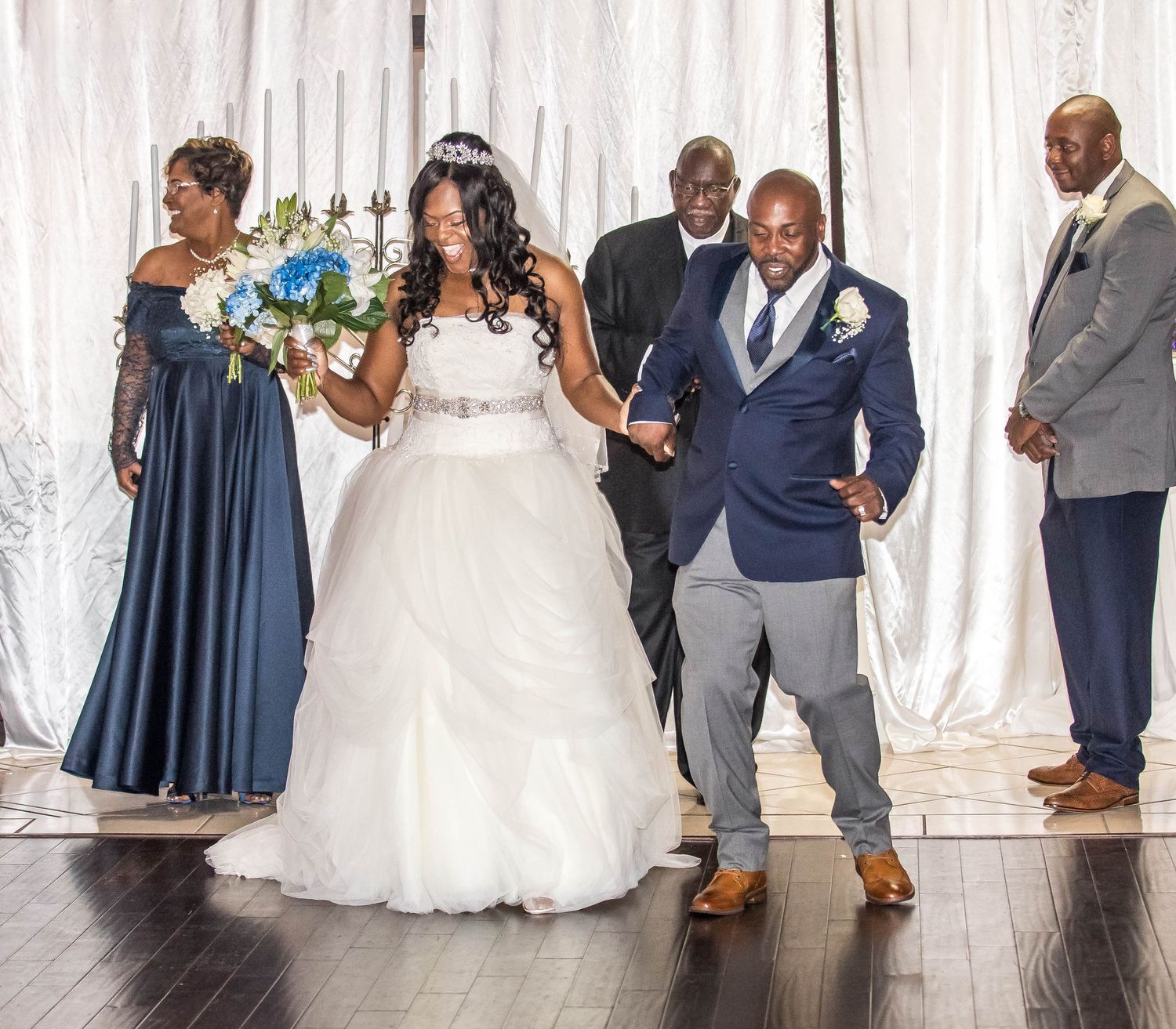 A bridal party poses together on a wooden floor against a white backdrop.