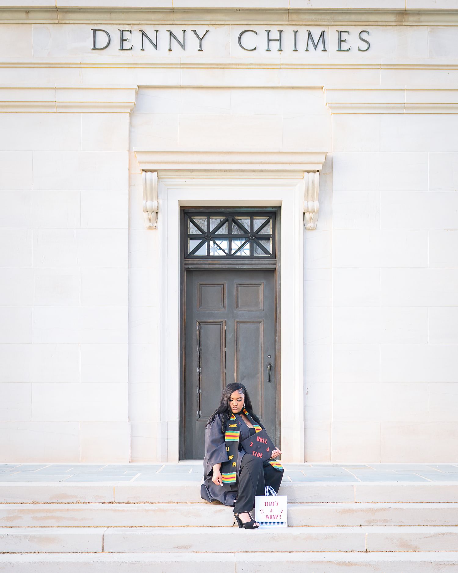 Person sitting on steps of white building with architectural columns and dark door reading book in natural light.