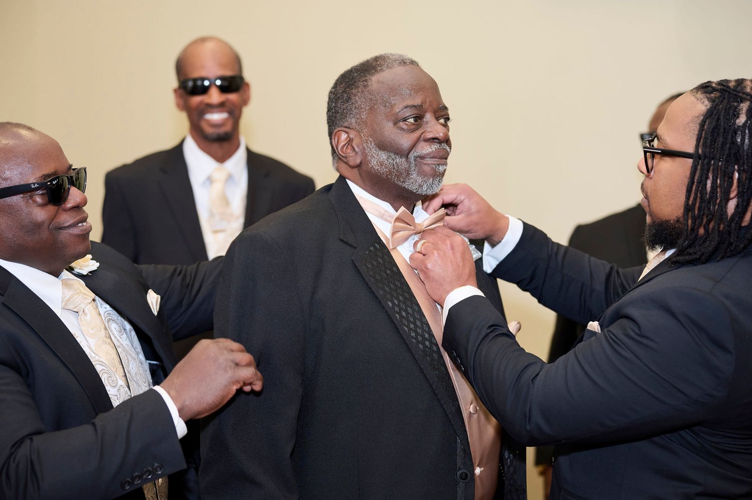 Three people in formal attire help adjust a necktie and prepare for a formal event.