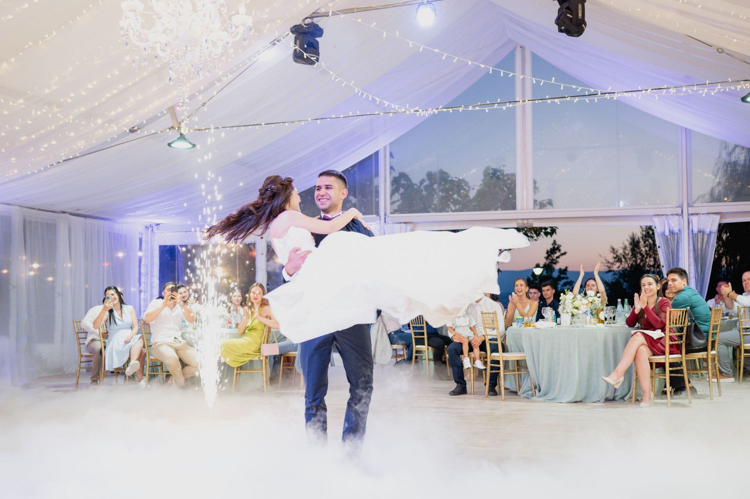 Panoramic view of wedding reception tent with string lights and dancing guests.