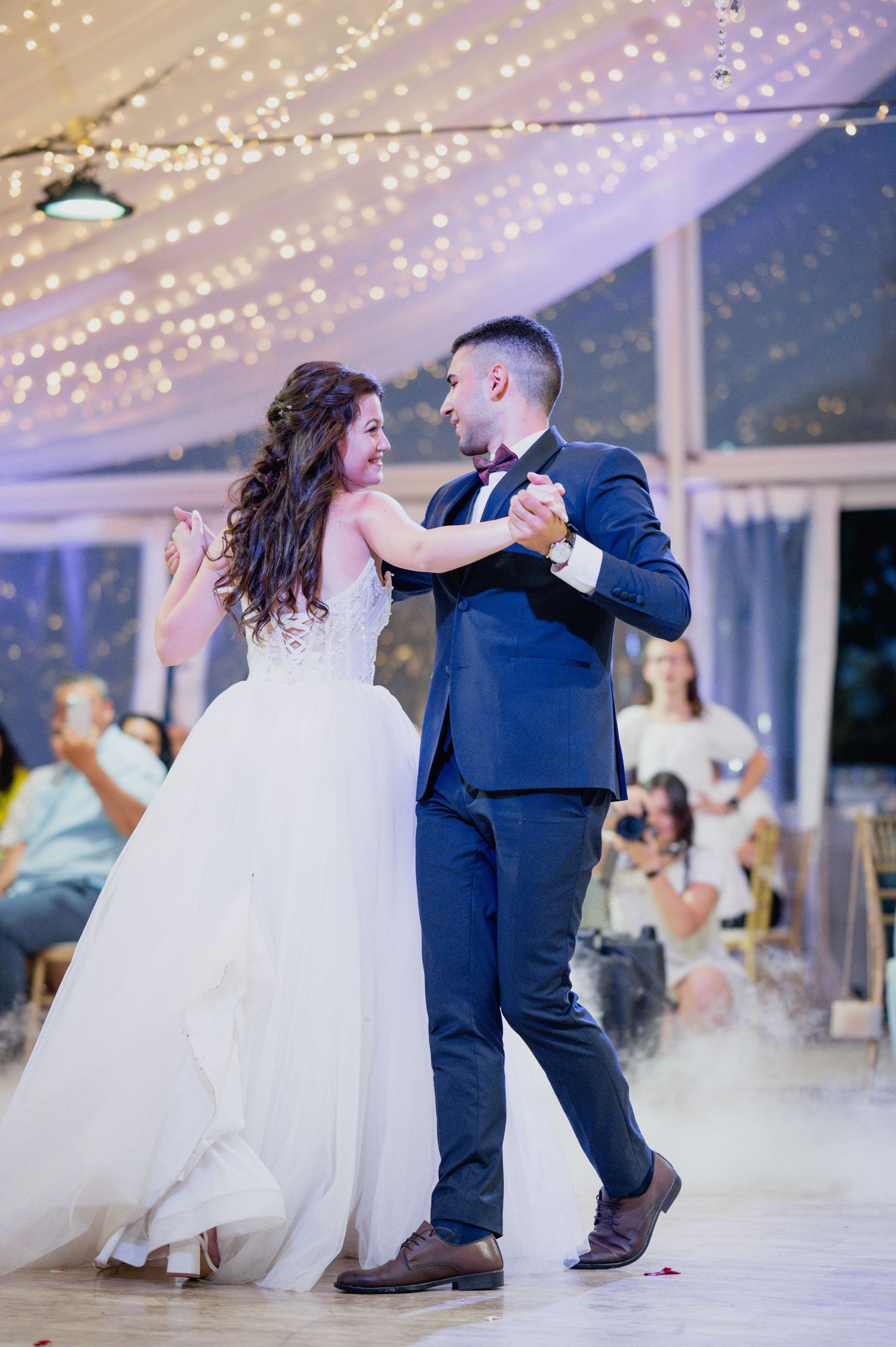 Couples dancing under romantic string lights at an elegant wedding reception.