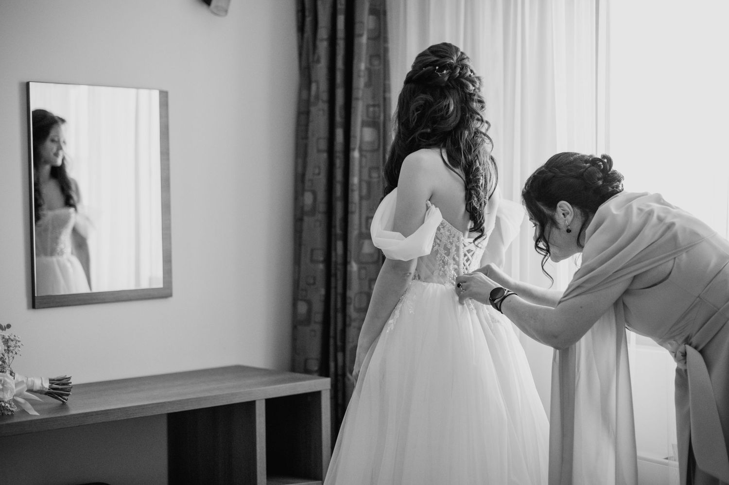 Wedding preparation scene showing final dress adjustments in a hotel room.