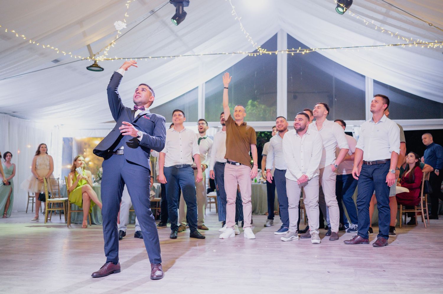 Wedding reception tent venue with string lights and guests gathered around the dance floor.