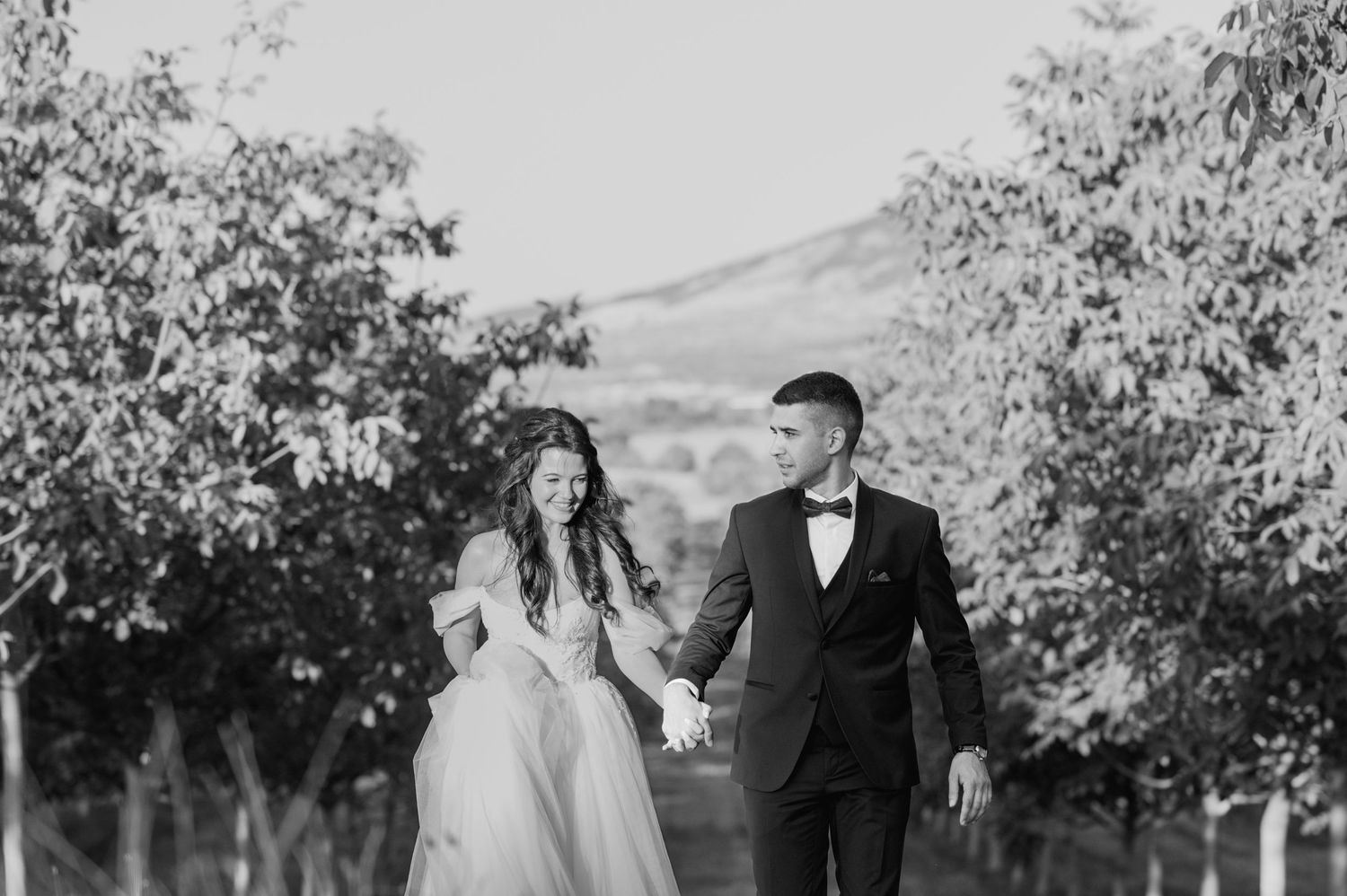 Wedding guests dance at an outdoor garden reception under trees at sunset.