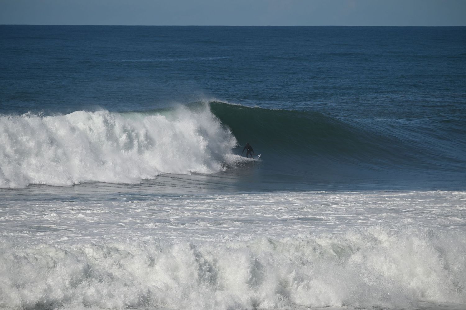 Surfer riding inside a massive barrel wave in the ocean on a sunny day.