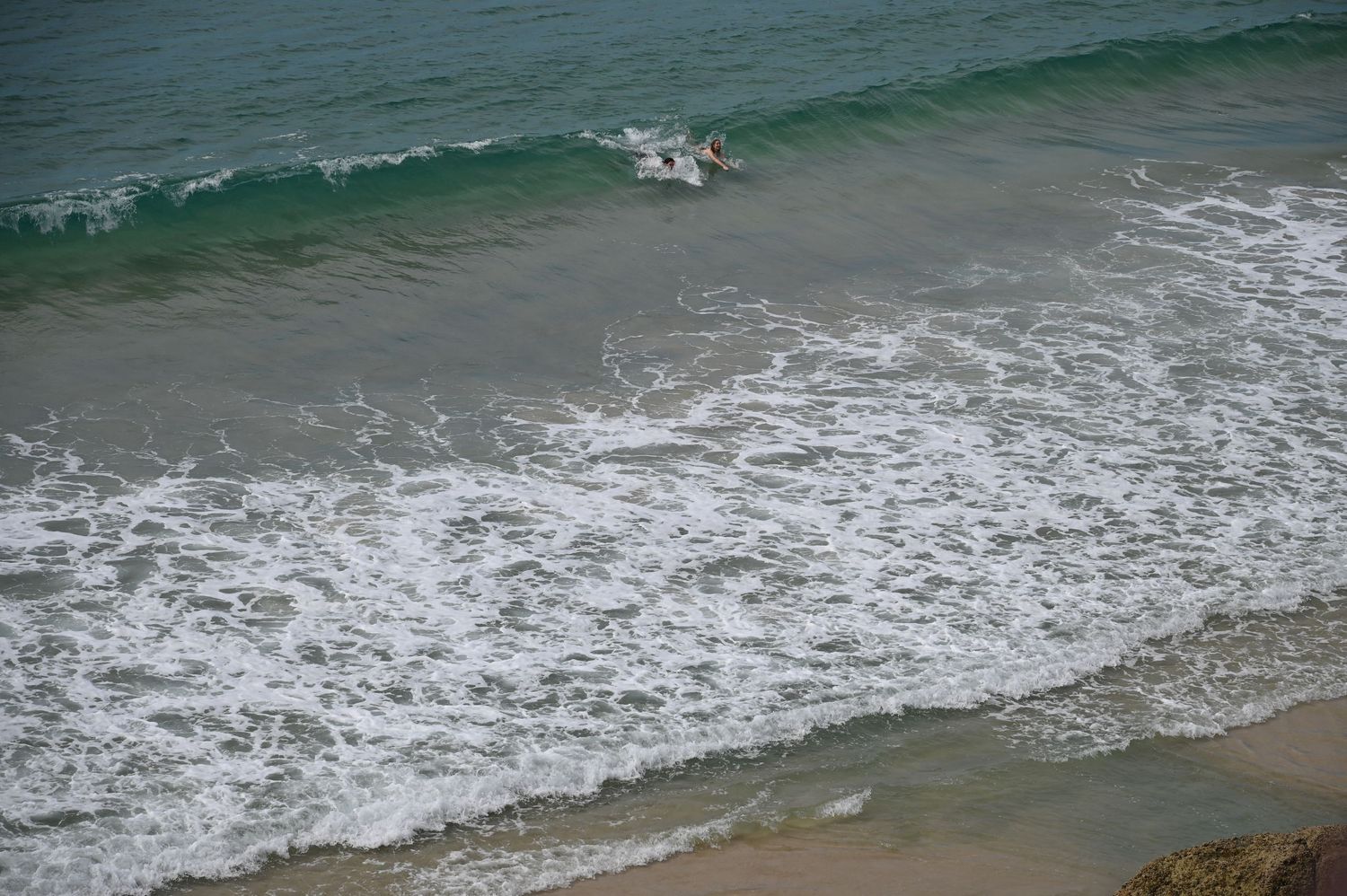 Aerial view of ocean waves crashing on a sandy beach with a surfer riding the turquoise water near the shoreline.