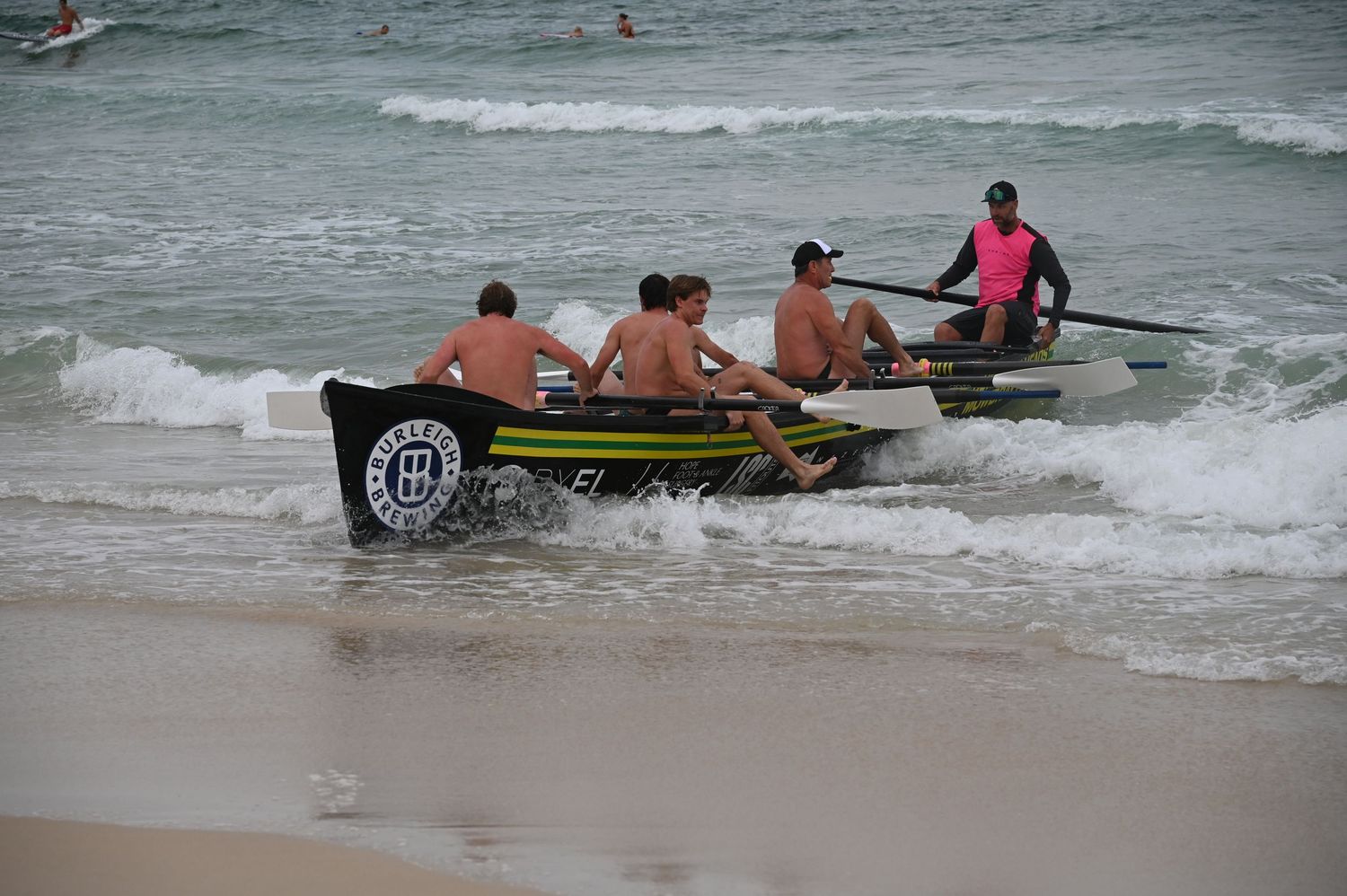 Surf lifesaving team rowing a boat through ocean waves at a beach competition.