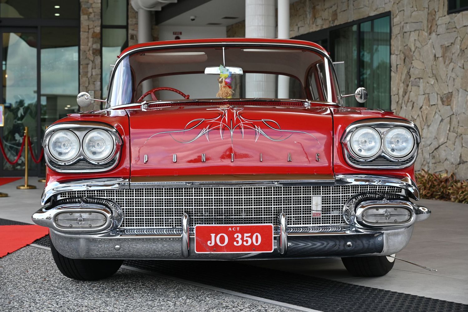 Red 1958 Chevrolet classic car with chrome grille and JO 350 license plate displayed at a car show.