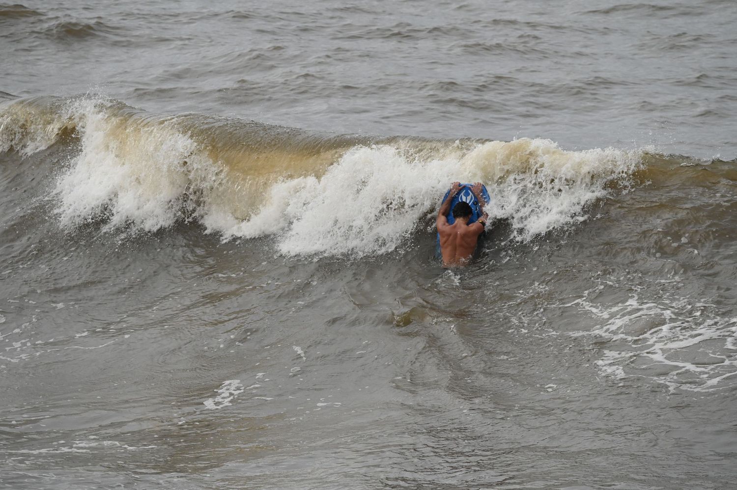 A bodyboarder paddling through a storm wave to get behind the break.