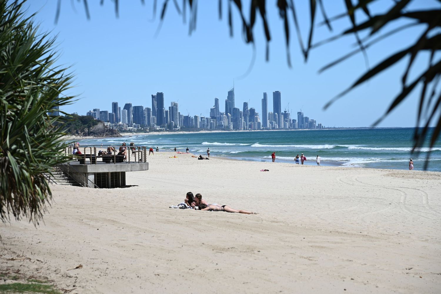 Sunbathers relax on a white sandy beach with Surfers Paradise skyline in the background on a sunny day.
