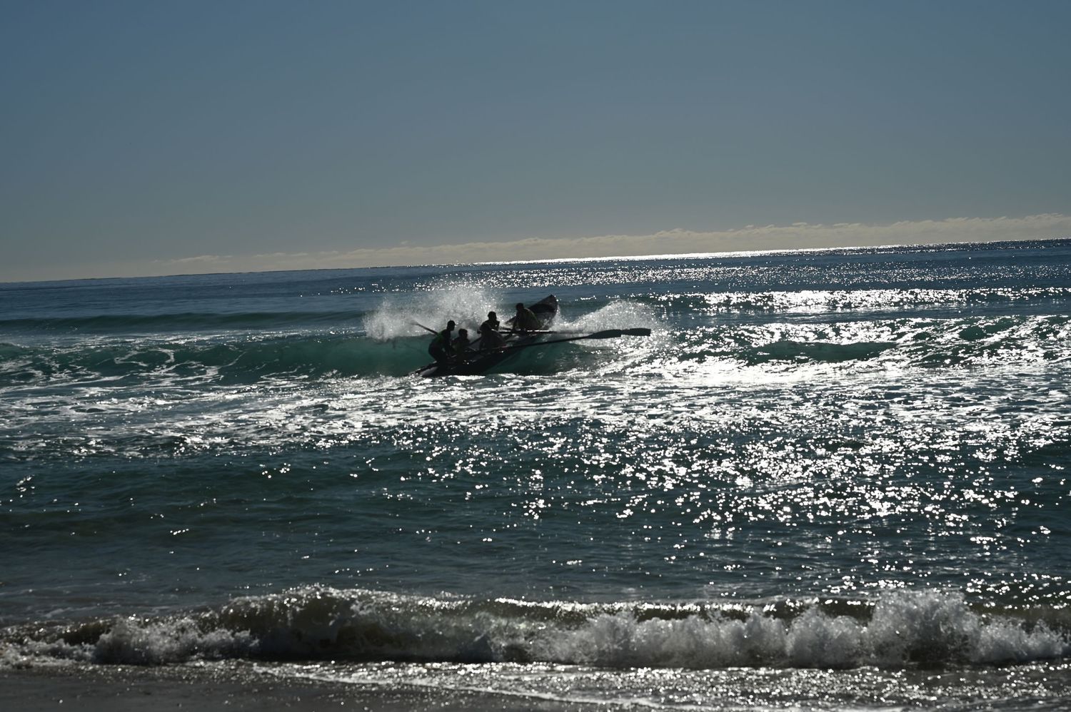 Inflatable rescue boat crashing through sparkling ocean waves with city skyline visible on bright sunny day.