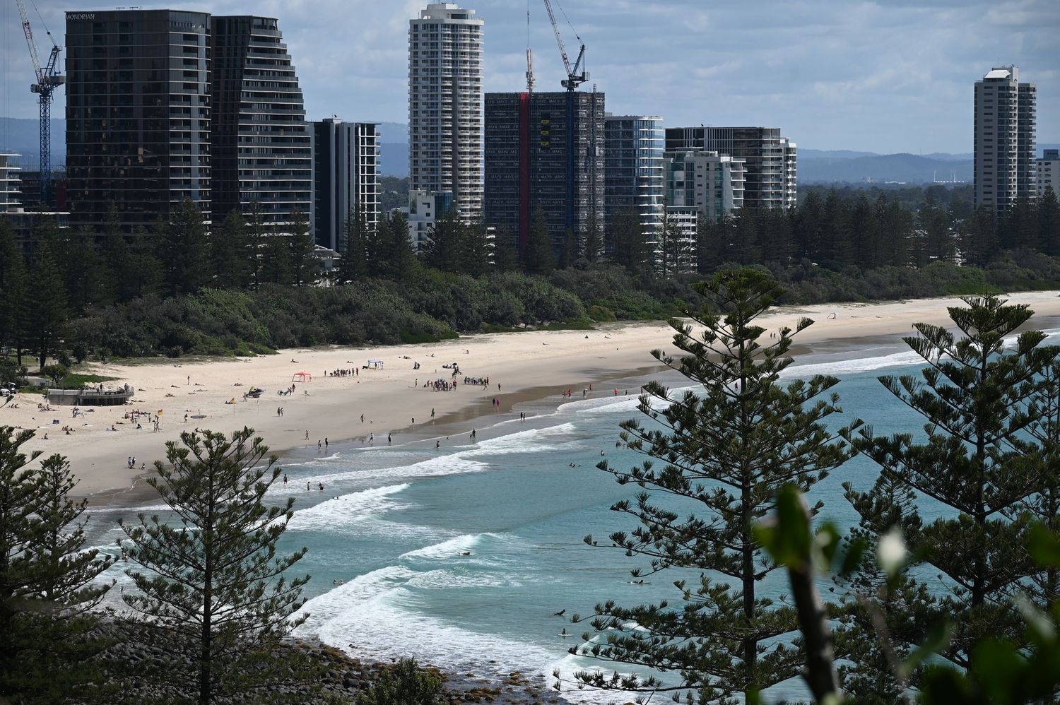 Aerial view of a sandy beach with high-rise buildings and cranes along the Gold Coast skyline in Australia.