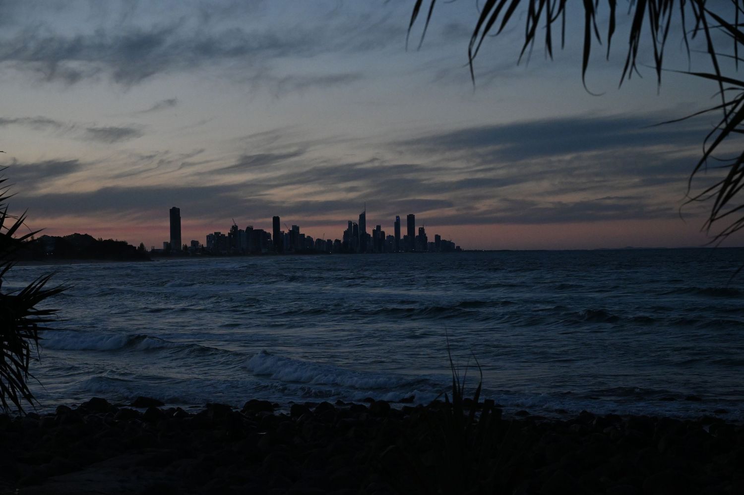 Dramatic dusk skyline view across choppy ocean waters with city silhouette against colorful sunset sky.