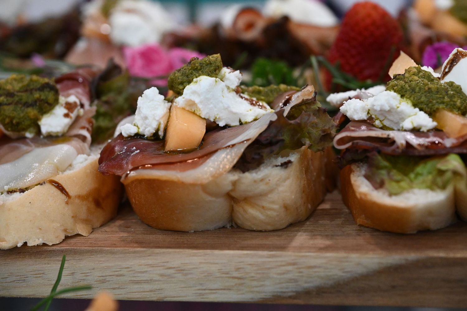 Gourmet bruschetta topped with prosciutto, goat cheese, and pesto on a rustic wooden board.