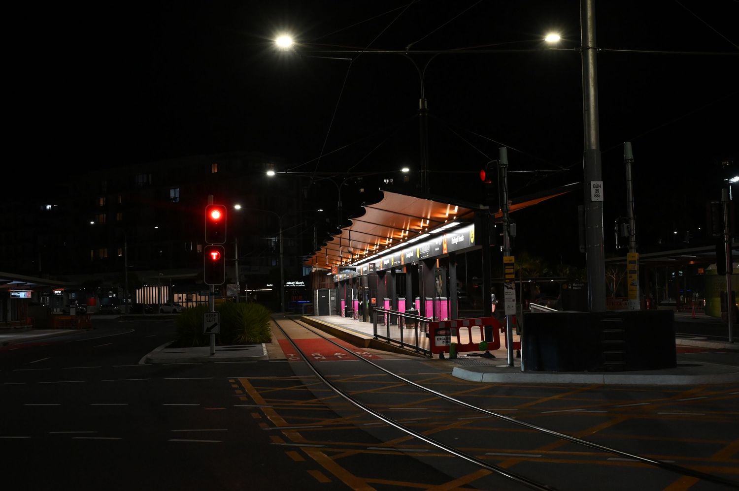 Illuminated tram station at night with red traffic lights and empty tracks in urban setting.