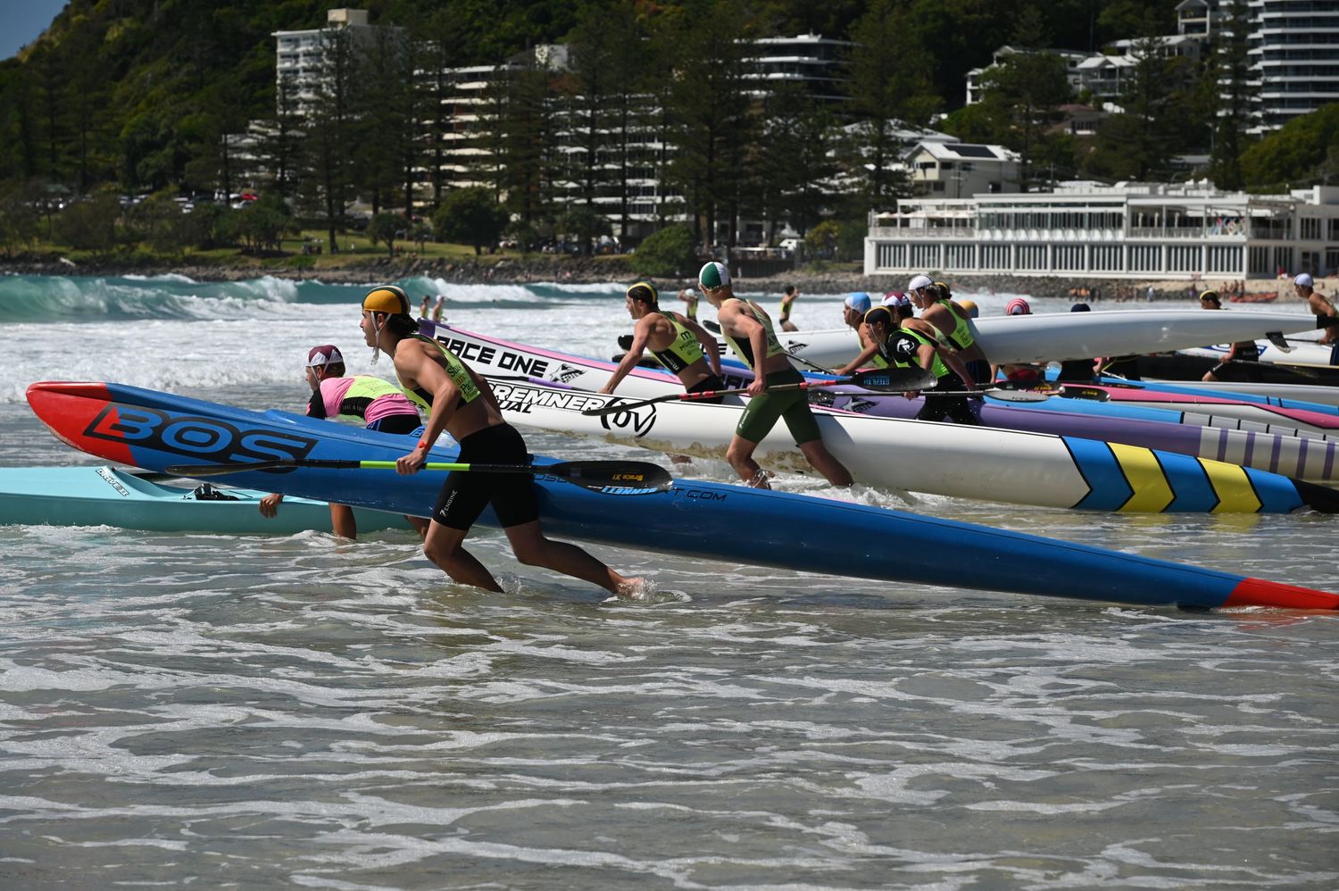 Competitors launch surf ski kayaks into ocean waves during a beach surf lifesaving race at an Australian coastal competition.