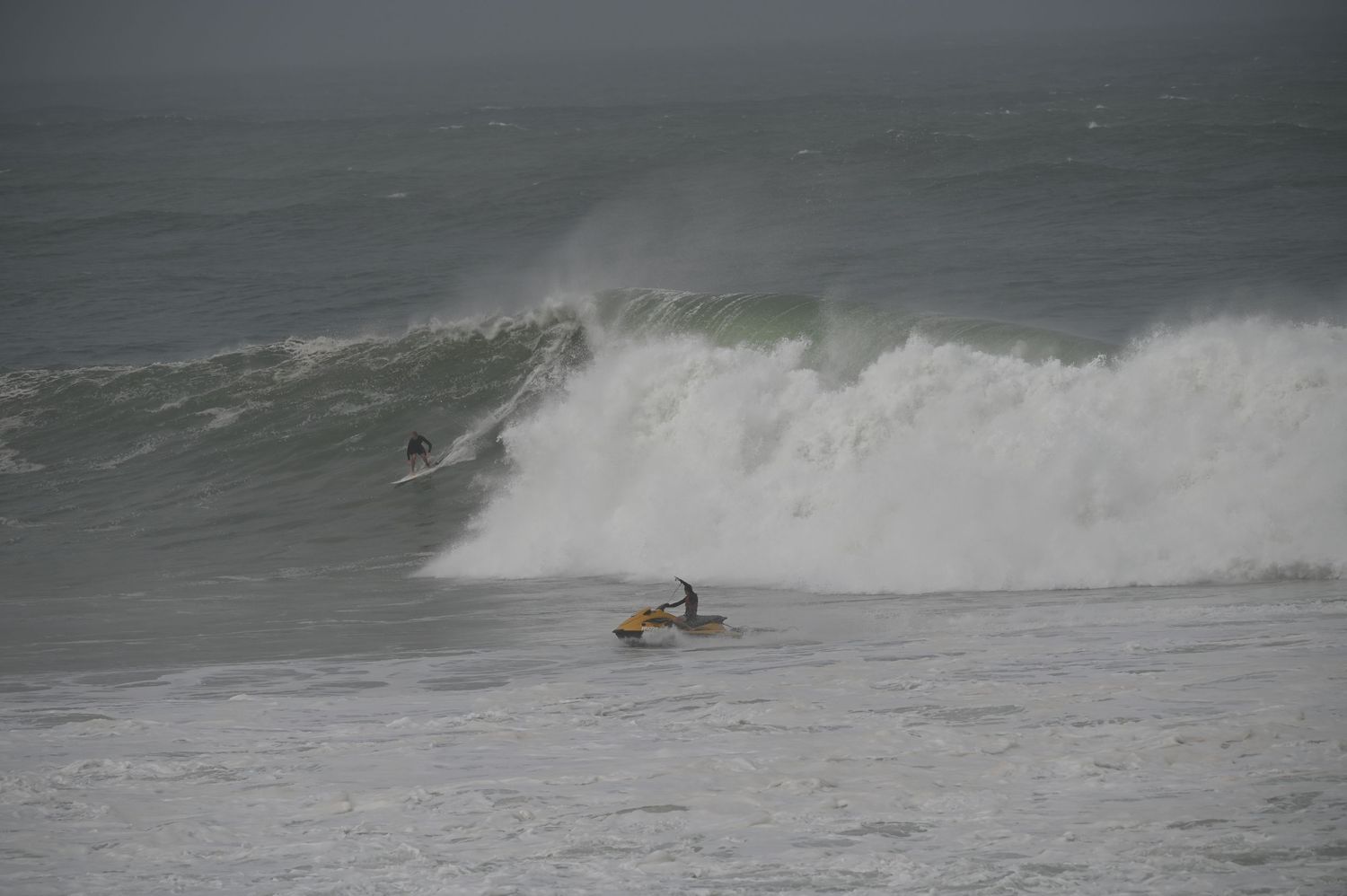Surfers paddling out to catch massive powerful waves on a stormy overcast day.