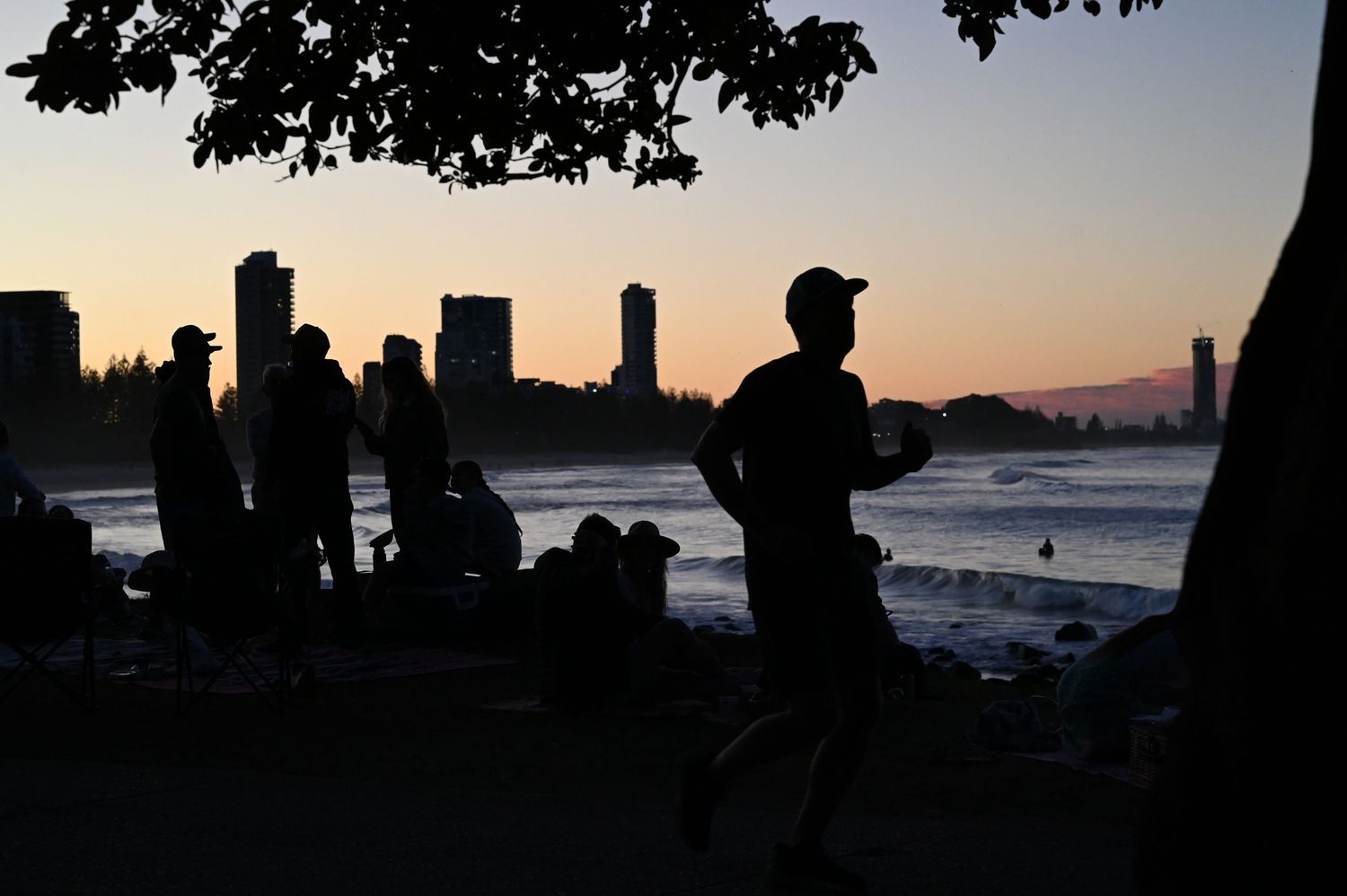 Silhouettes of people and city skyscrapers against a colorful orange sunset sky at the beach.