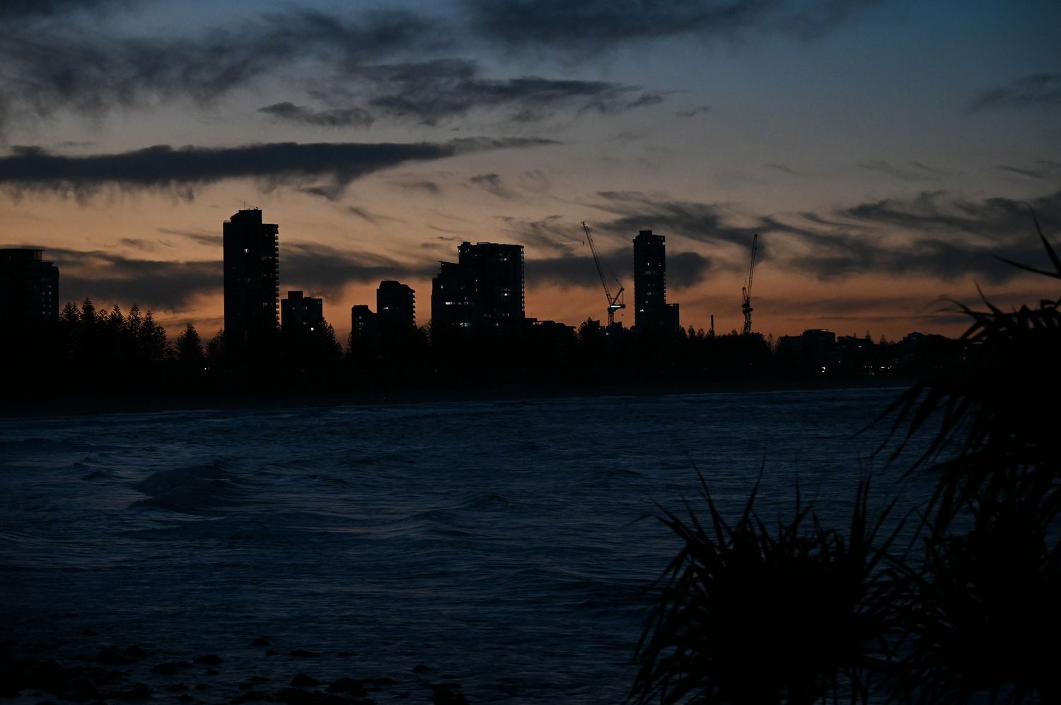 City skyline silhouetted against a dramatic orange and blue sunset sky reflecting over calm water at dusk.