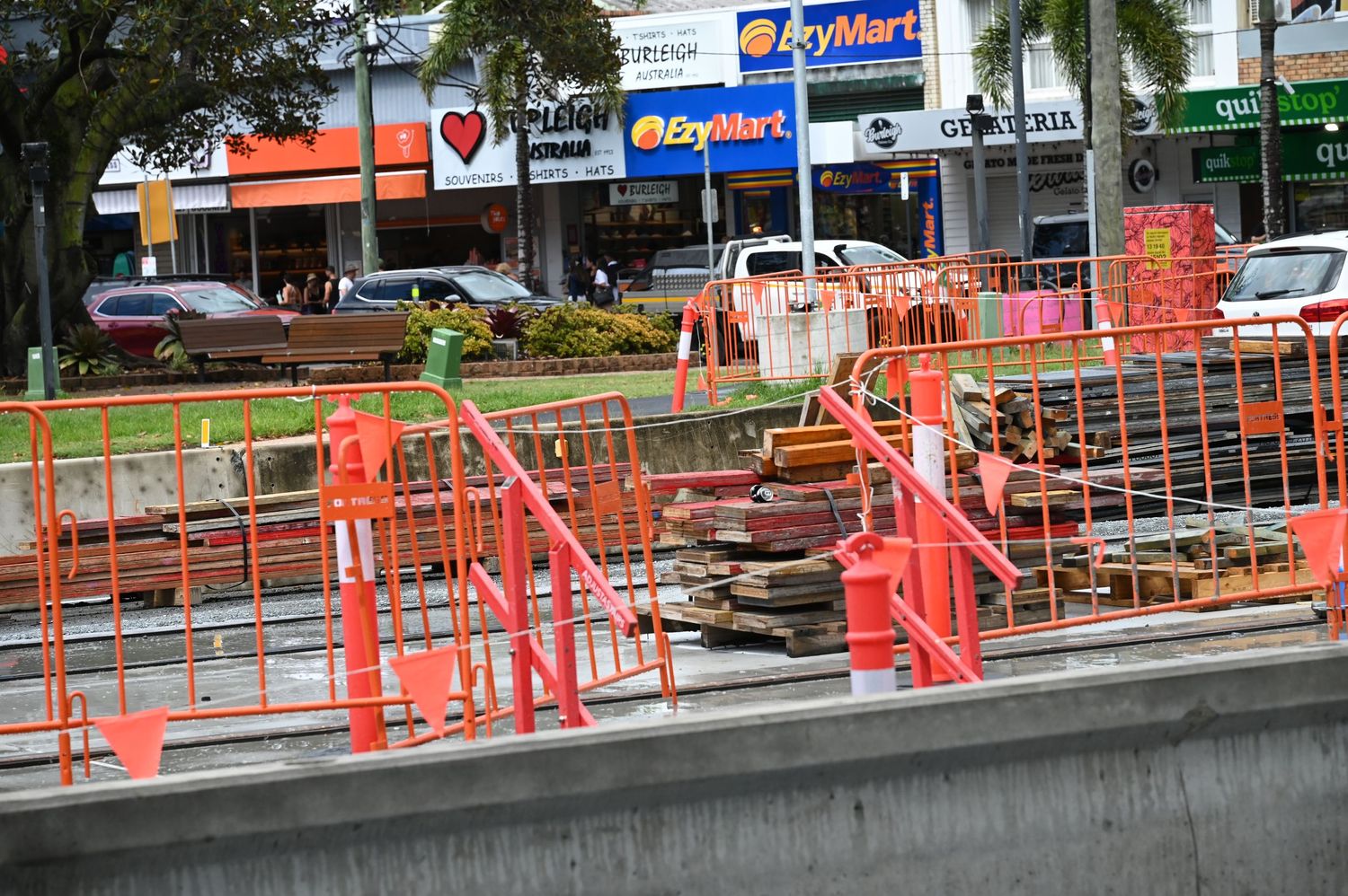 Orange construction barriers surround a roadwork site near a busy shopping strip with PriceSmart and other retail stores.