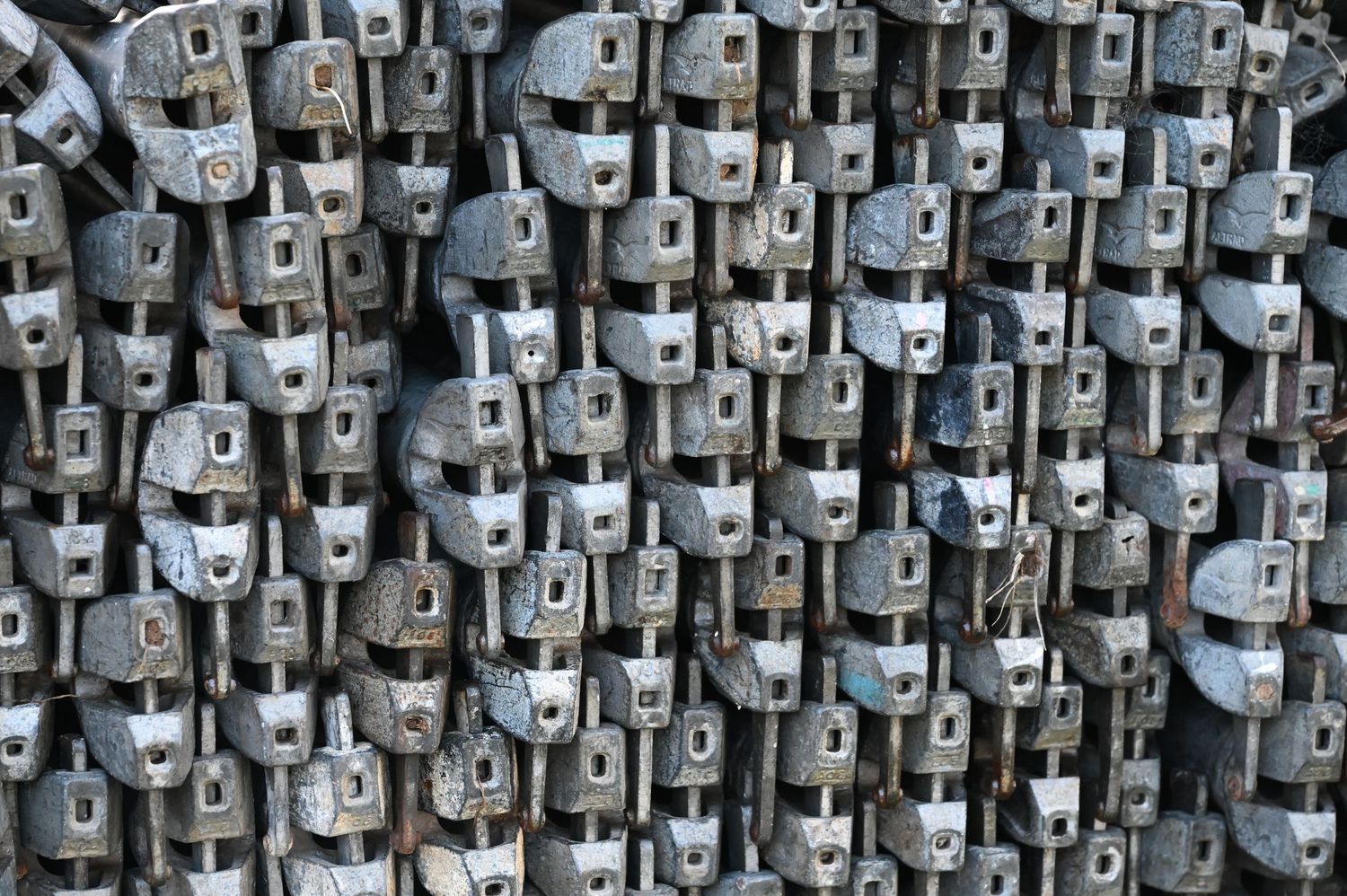 Large collection of stacked gray metal industrial fasteners and brackets arranged in dense rows.