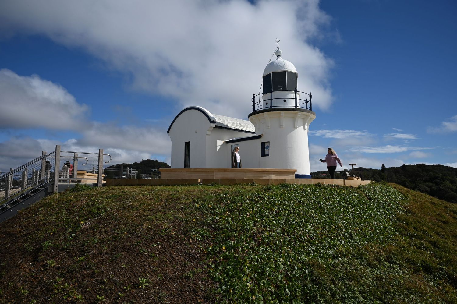 White lighthouse and keeper's cottage on a green hill under blue skies with clouds.
