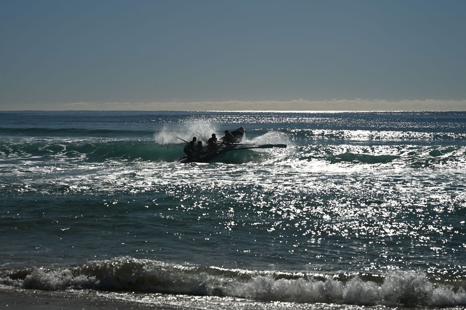 A motorboat navigating through sparkling ocean waves near a sunny beach shoreline.