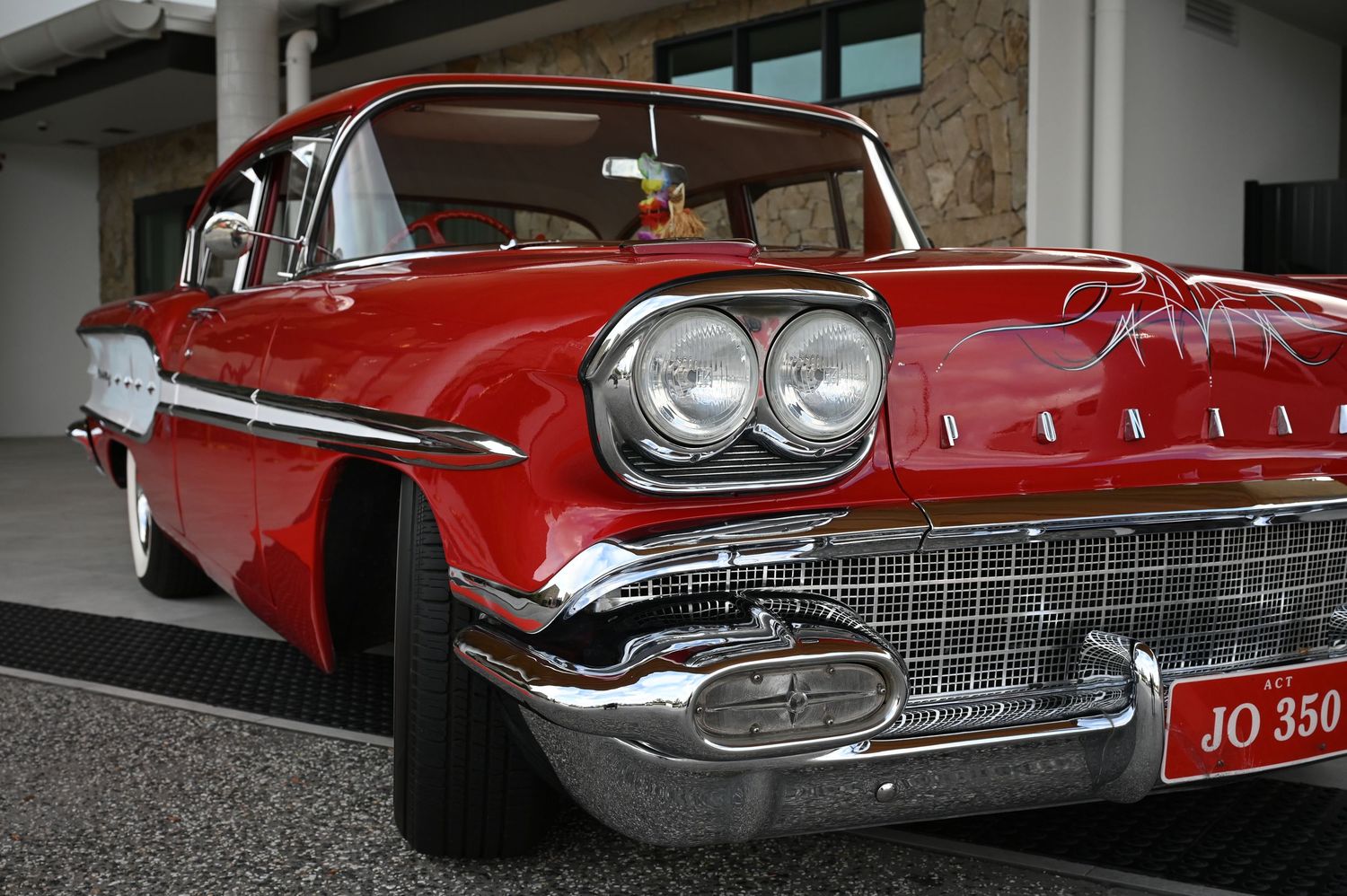 Vintage red 1958 Pontiac classic car with chrome grille and dual headlights, license plate JO 350, parked outside.
