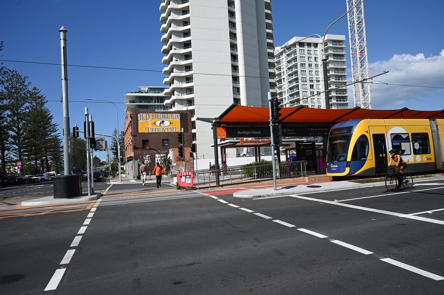 Modern light rail tram at Gold Coast station with high-rise buildings and pedestrian crossing on a sunny day.