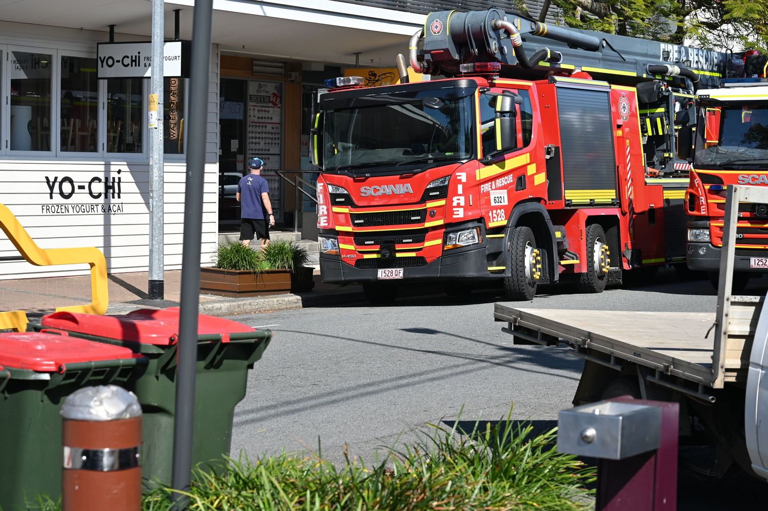 Red Scania fire truck responding to an emergency outside a Yo-Chi frozen yogurt shop in a suburban shopping center.