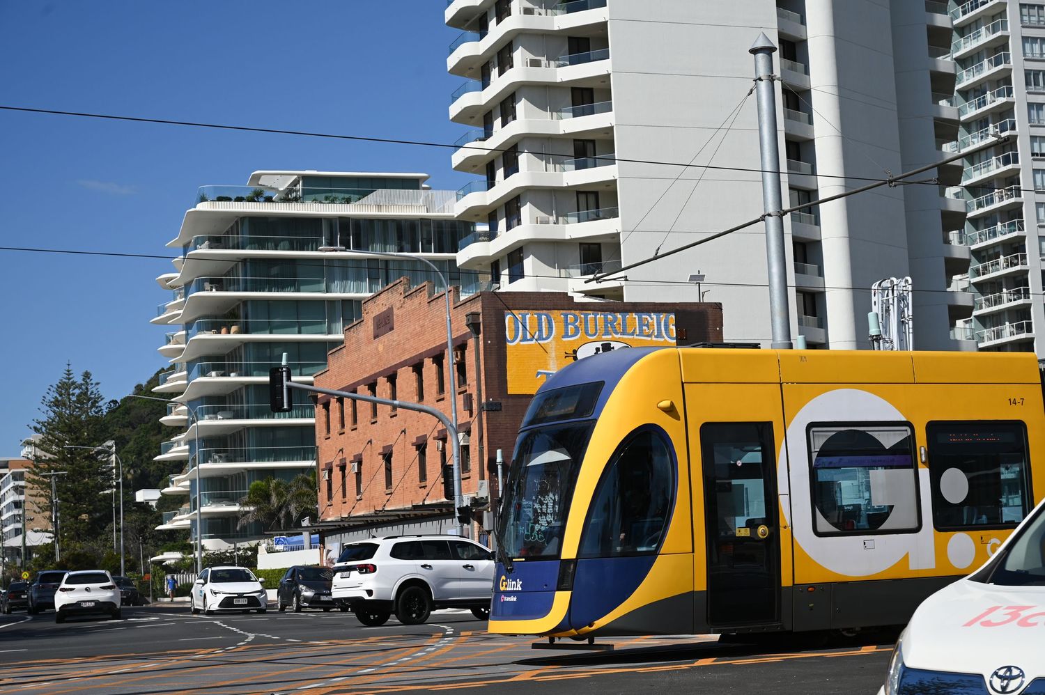 Yellow tram on Gold Coast light rail network passing through busy intersection with modern high-rise buildings in background.