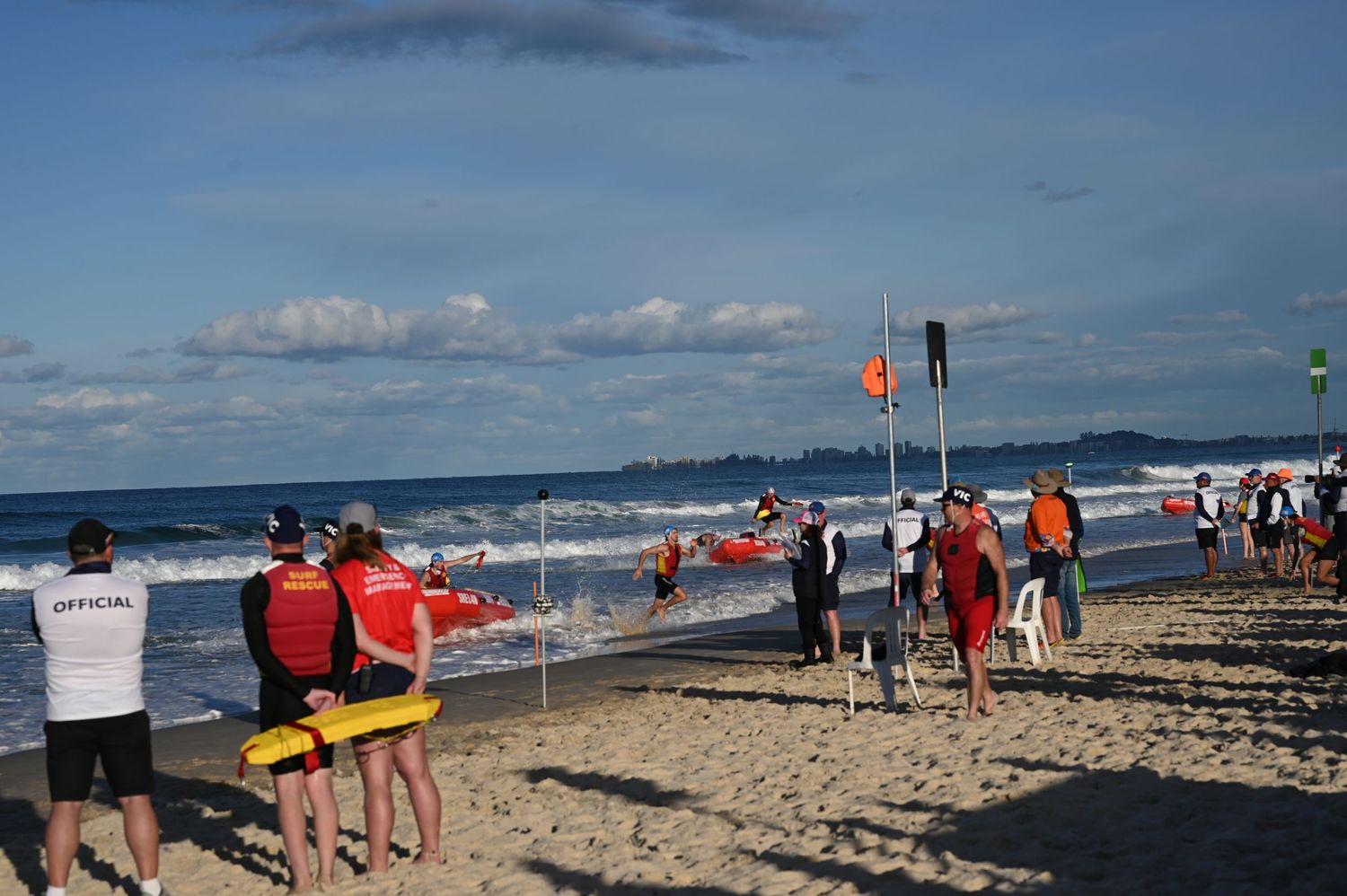 Surf lifesaving competition participants and officials gathered on a sandy beach near the ocean.