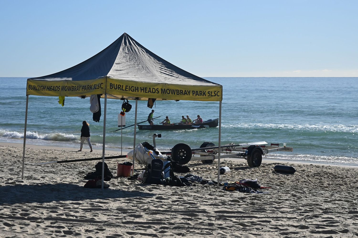 Burleigh Heads Mowbray Park SLSC tent on sandy beach with ocean waves and surf lifesaving equipment nearby.