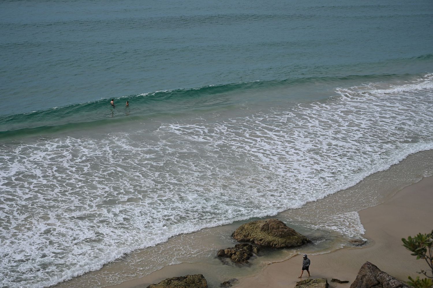 Aerial view of a tropical beach with turquoise waves, sandy shore, and people wading in the ocean.