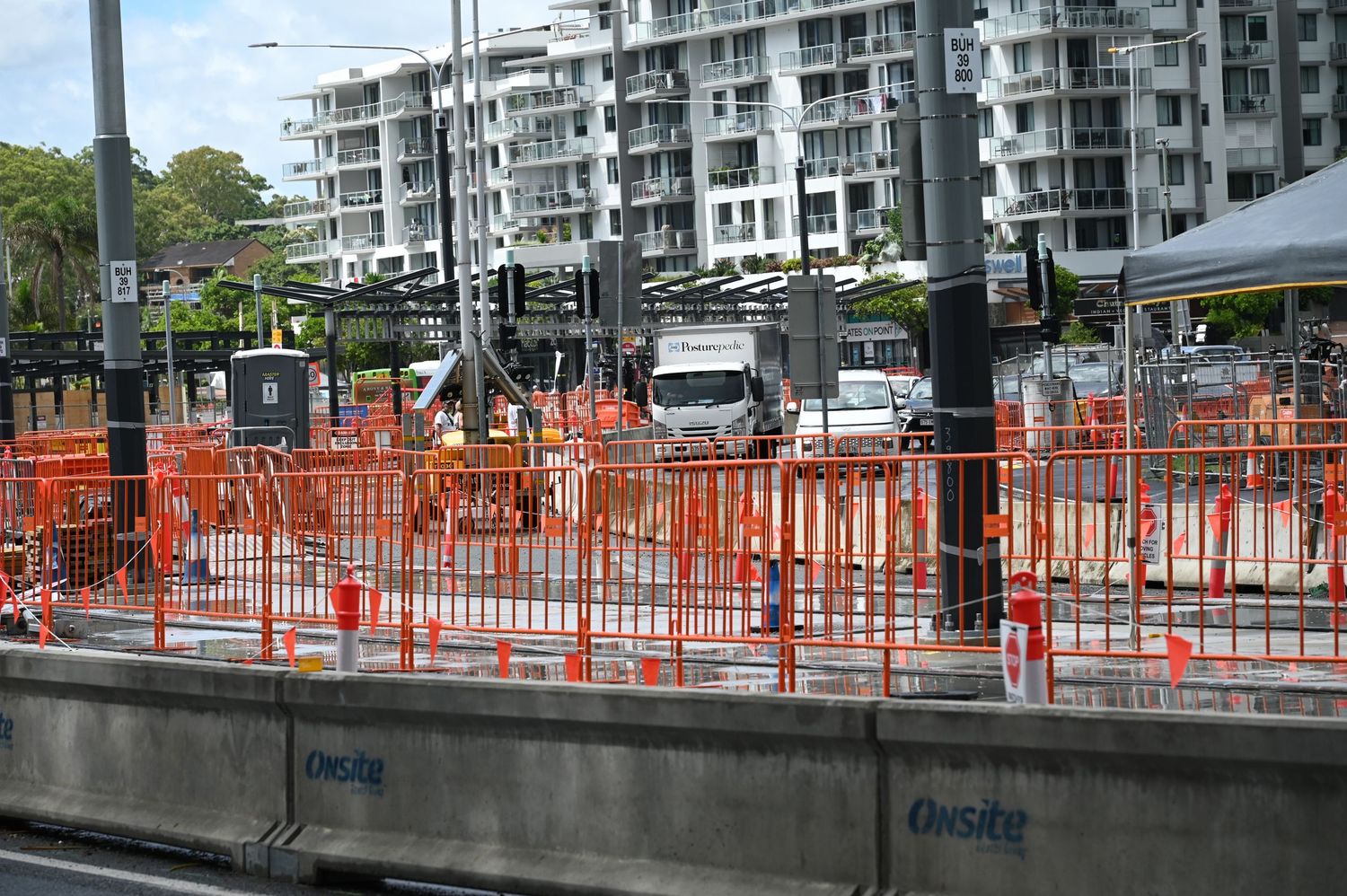 Construction site with orange safety fencing barriers near urban apartments and trucks in Australia.