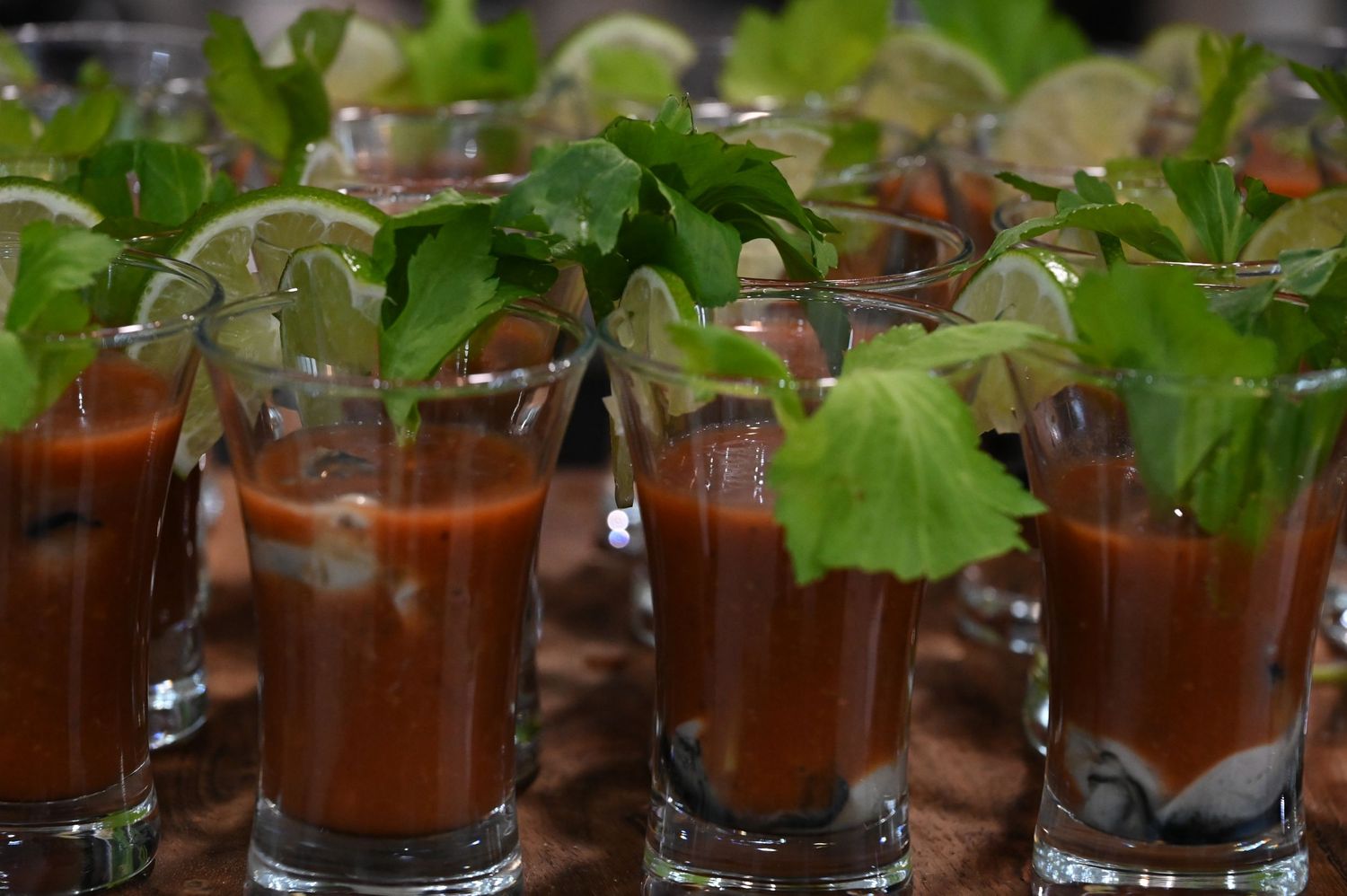Bloody Mary shots garnished with fresh cilantro and lime slices served in small glasses at a catered event.