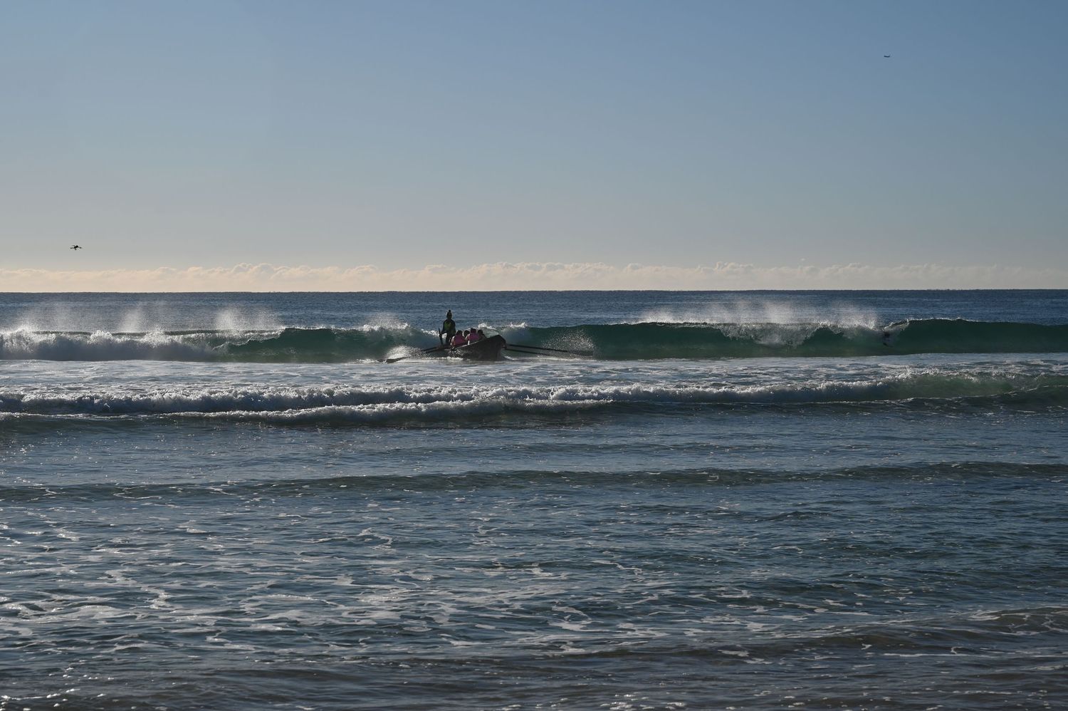 Surfer riding ocean waves on a clear day at a sandy beach with calm blue skies in the background.